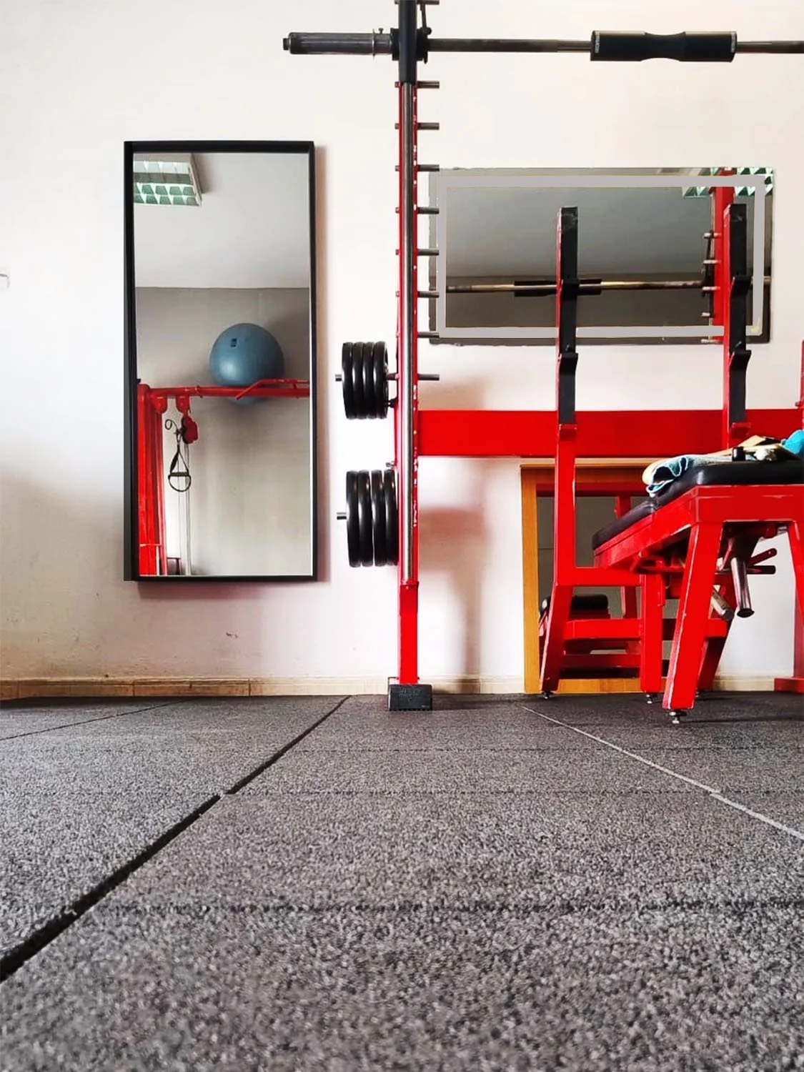 Equipamiento de gimnasio con espejo, pesas, barra para levantamiento de pesas y máquina de entrenamiento de fuerza en interiores.