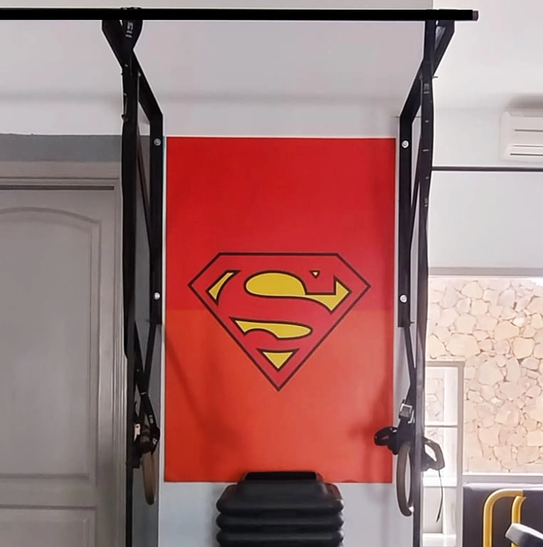 Una pared con un logo de Superman en un gimnasio, con colchonetas y bandas de ejercicio colgadas.
