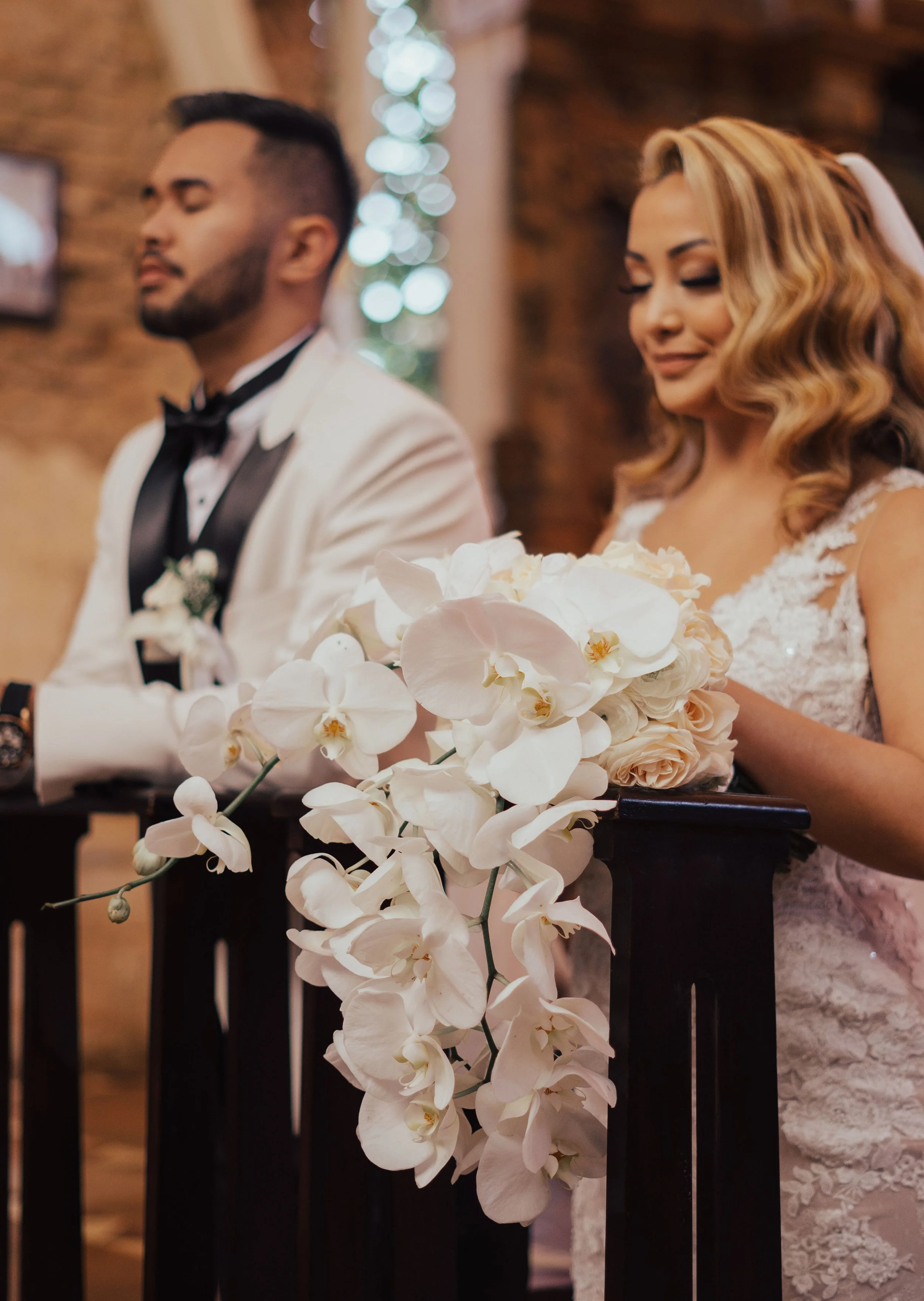 A bride and groom standing at an altar during their wedding ceremony, with a bouquet of white orchids and roses in front of them.