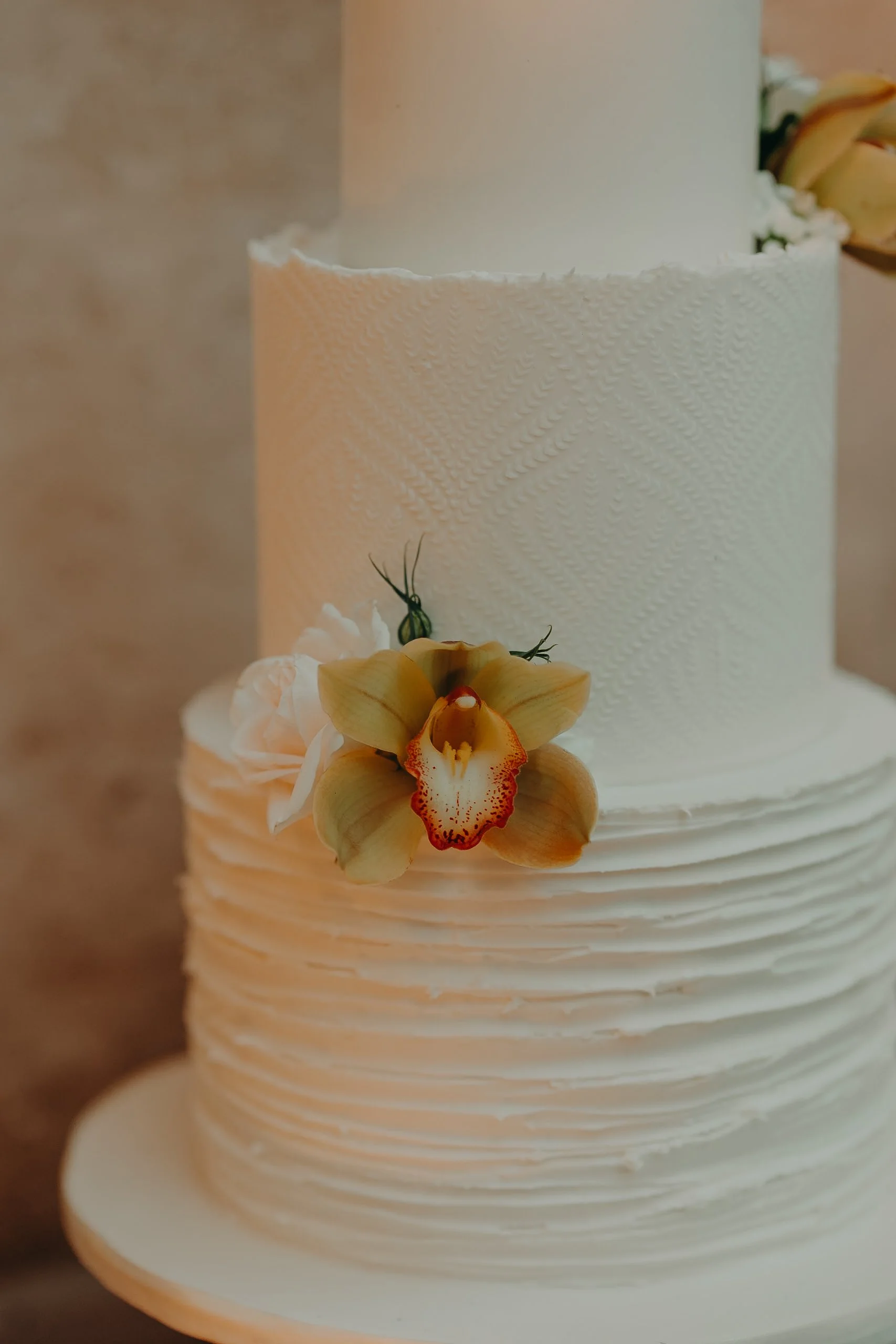 White wedding cake with textured icing and a large yellow orchid flower decoration.