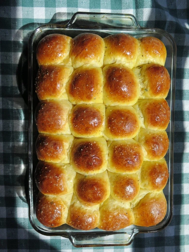 Freshly baked dinner rolls in a glass baking dish on a checkered tablecloth.