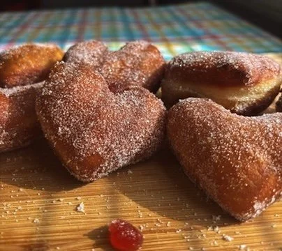 Heart-shaped sugared pastries on a wooden surface with a colorful checkered tablecloth in the background.