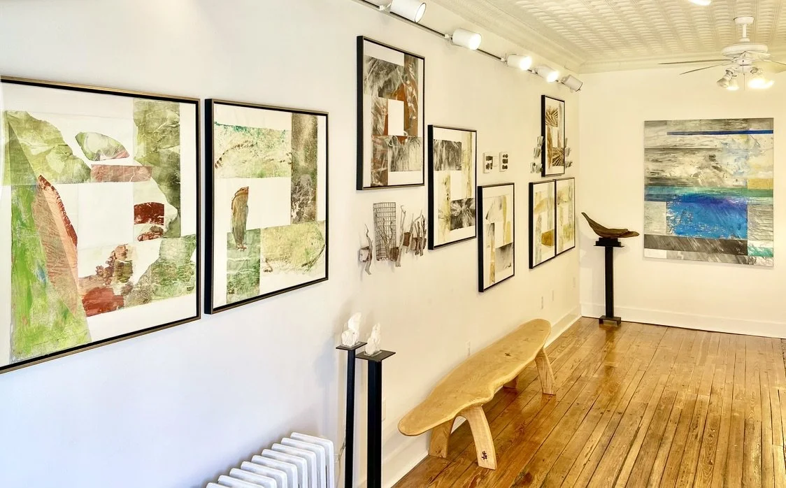 Interior of an art gallery with colorful paintings on white walls and hardwood floors.