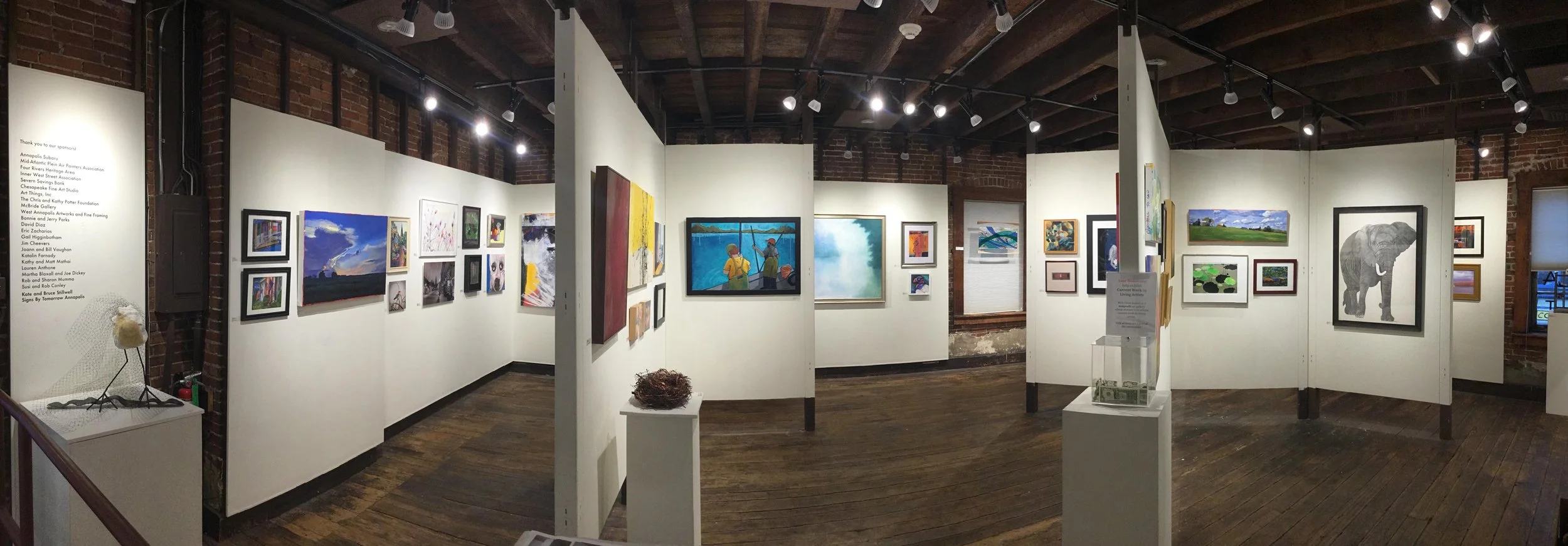 An art gallery with three sculptures of human figures and framed photographs on the wall.