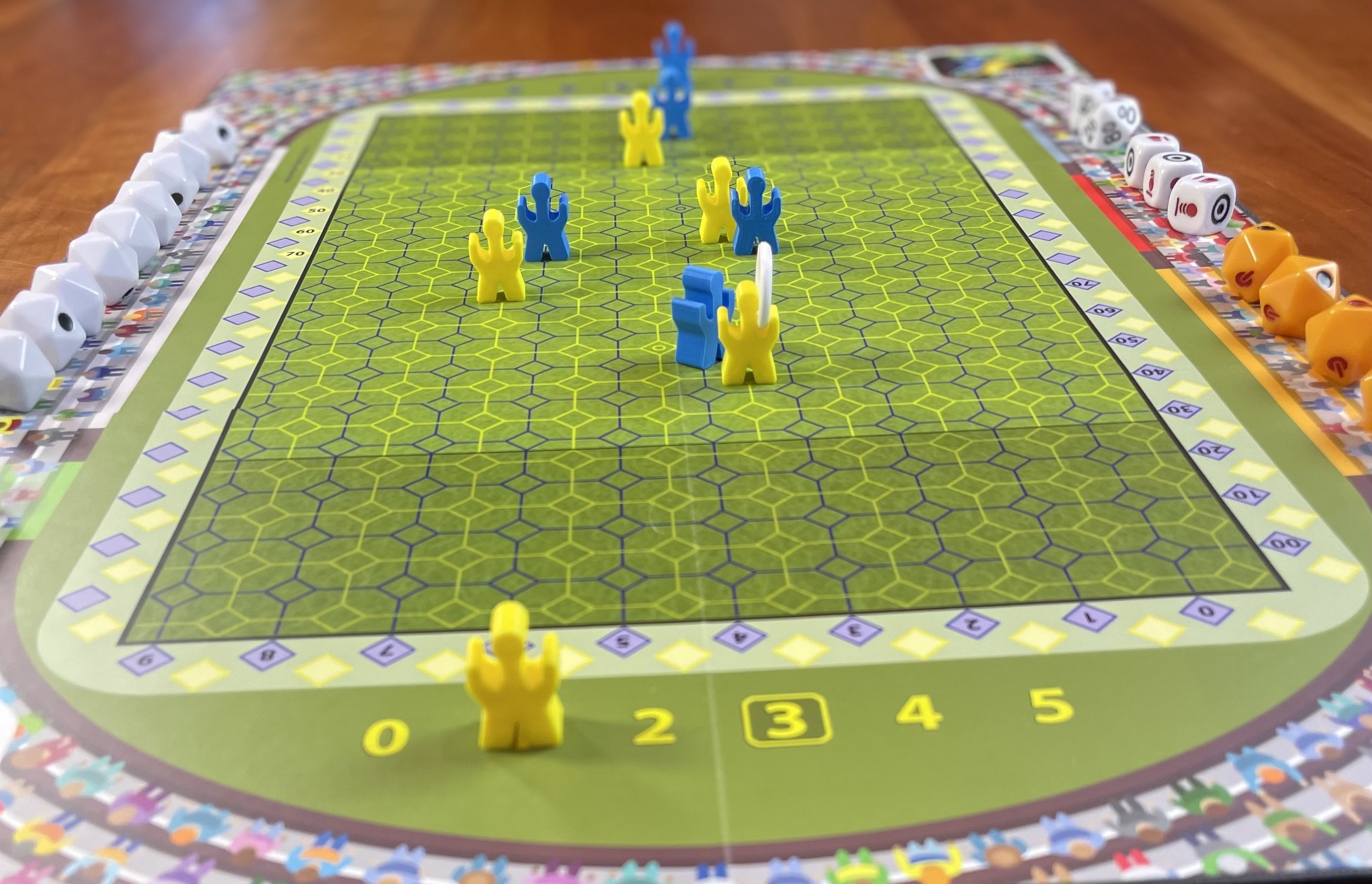 Close-up of a board game with hexagonal grid, featuring blue and yellow player pieces, surrounded by various colored dice on the sides.