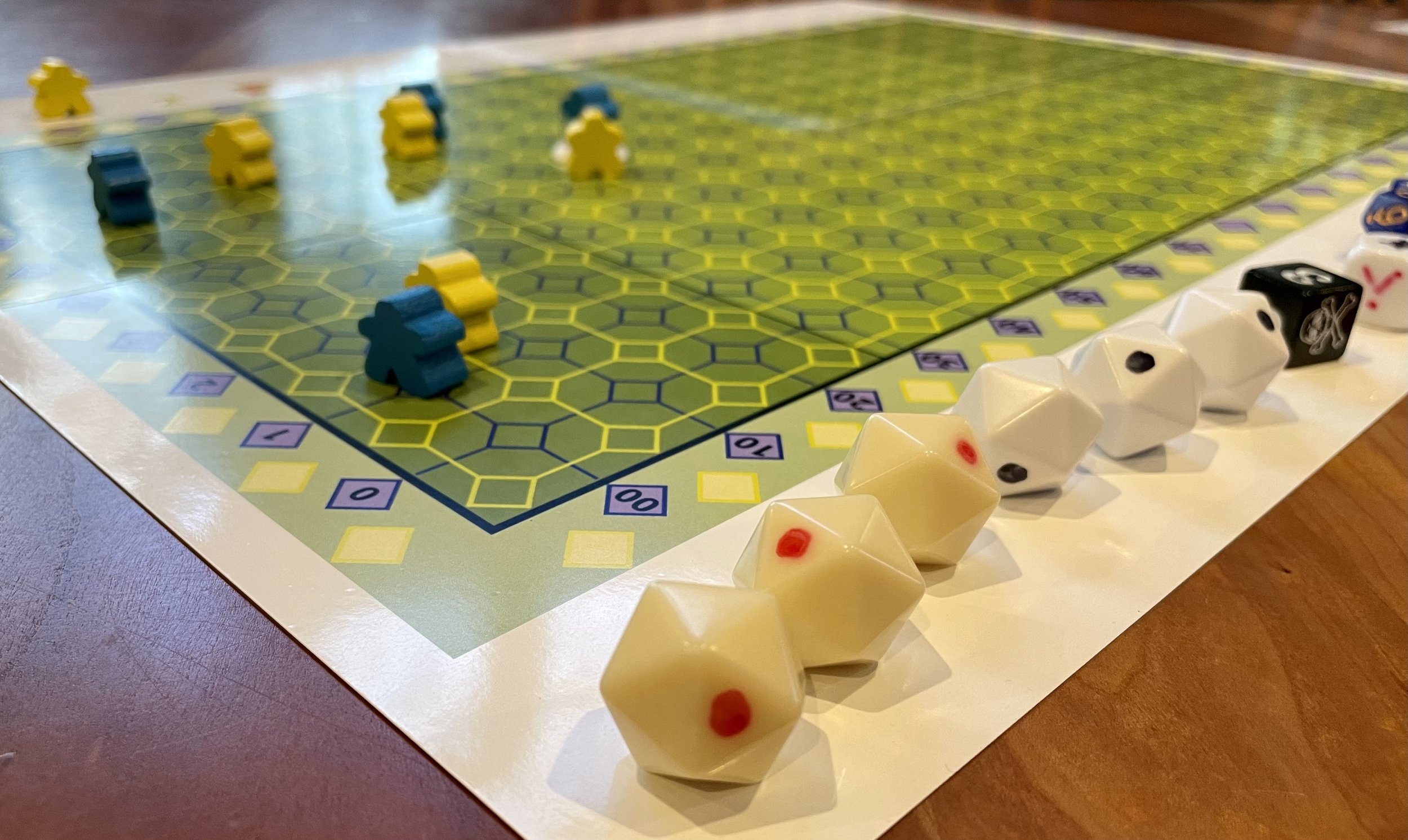 Board game setup with a hexagonal grid, yellow and blue meeples, and multi-sided dice on a wooden table.