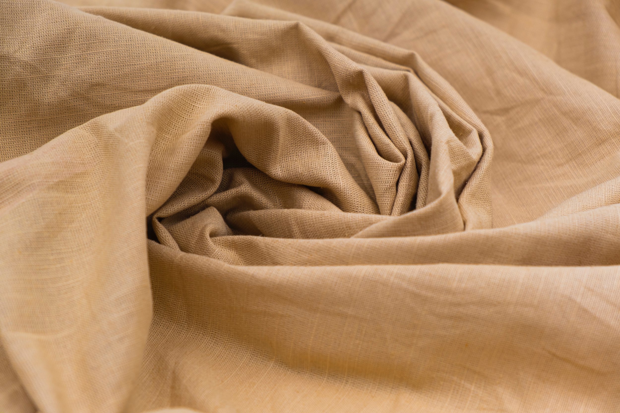 A close-up view of beige fabric with a textured, slightly wrinkled surface, casually draped and folded.