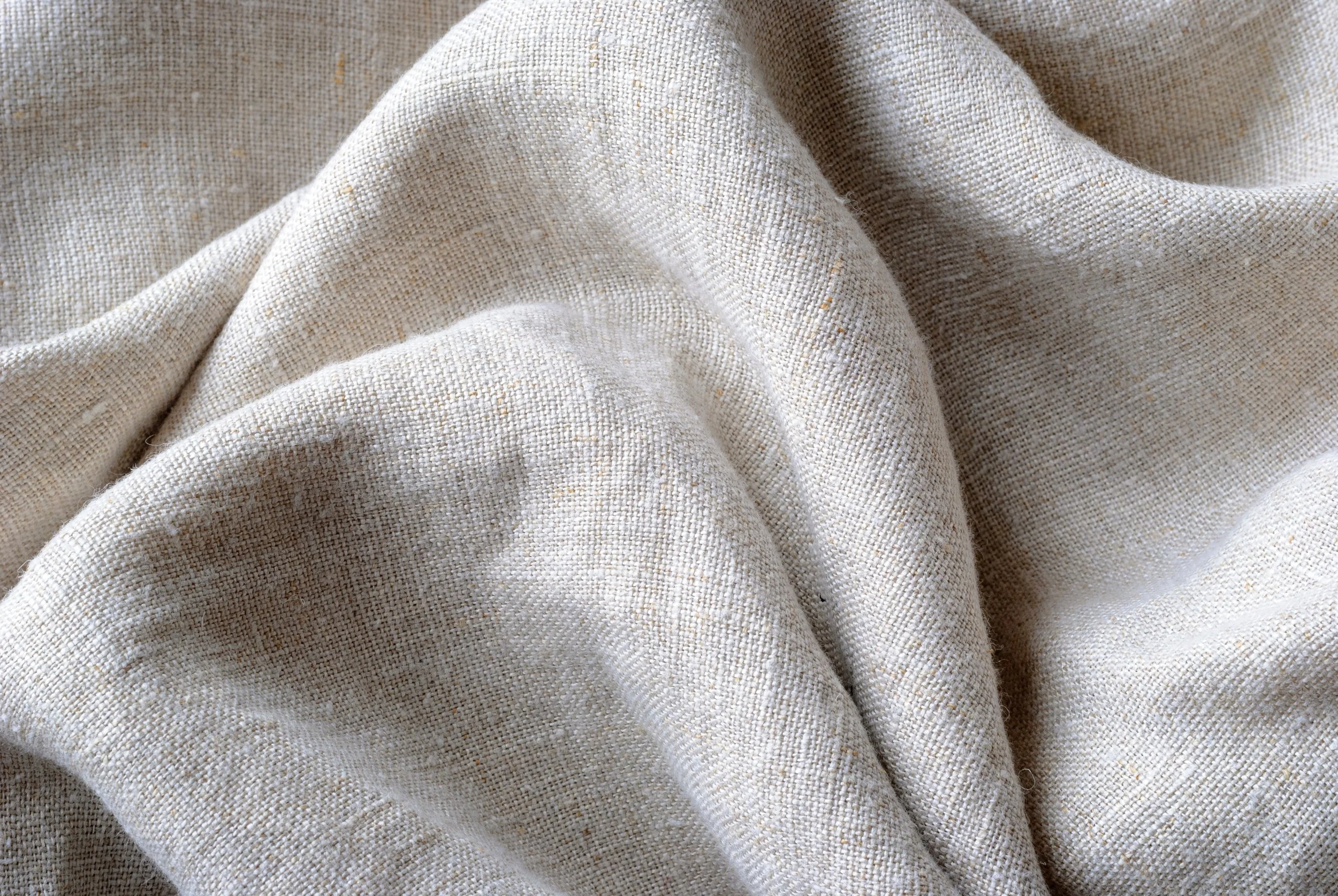 Close-up of beige fabric with a textured woven pattern, draped with soft folds.