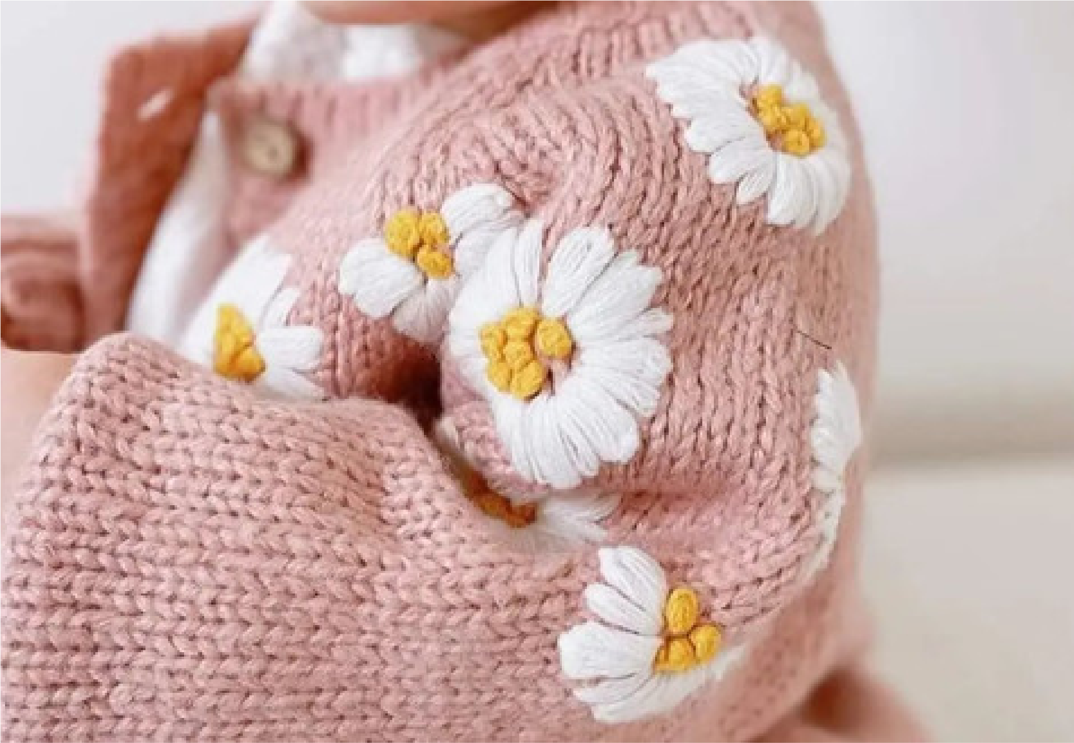 Close-up of a person's arm wrapped in a pink knitted sweater with white daisy flower appliques that have yellow centers.