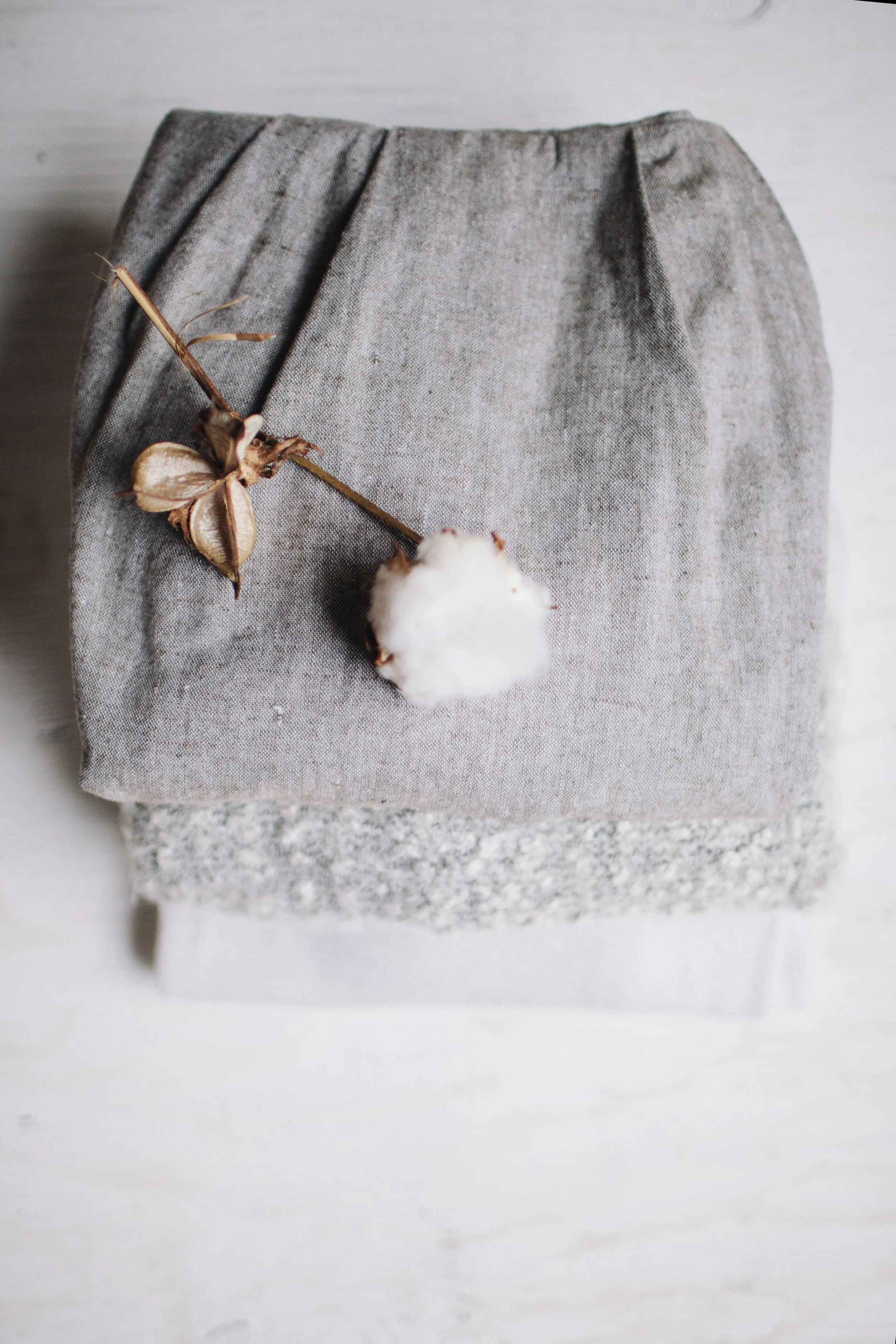 Gray fabric pouch with a dried cotton branch and cotton boll on top of it, placed on a light-colored surface.