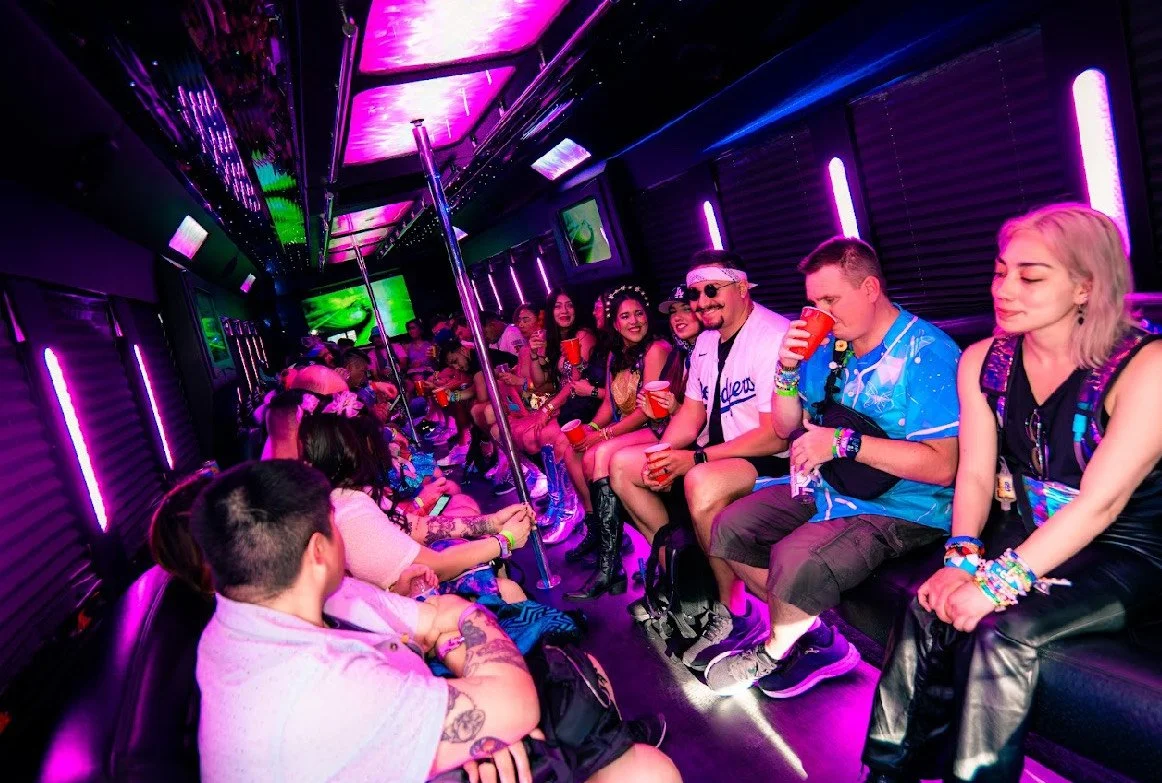 People sitting in a party bus decorated with neon purple and pink lights, holding drinks, and enjoying themselves.