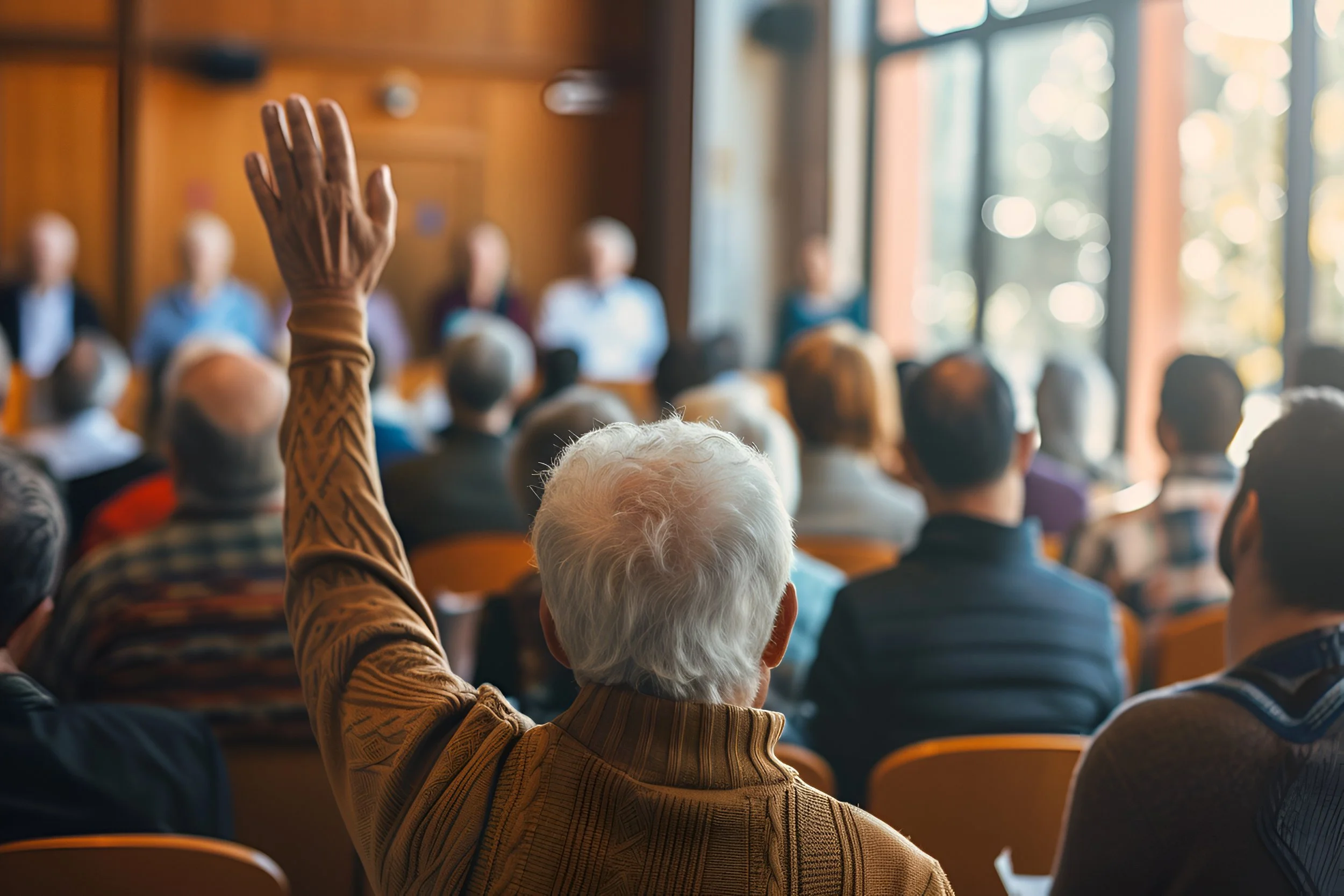 Older gentleman raised his hand from the back of the room as a panel takes questions in the front.