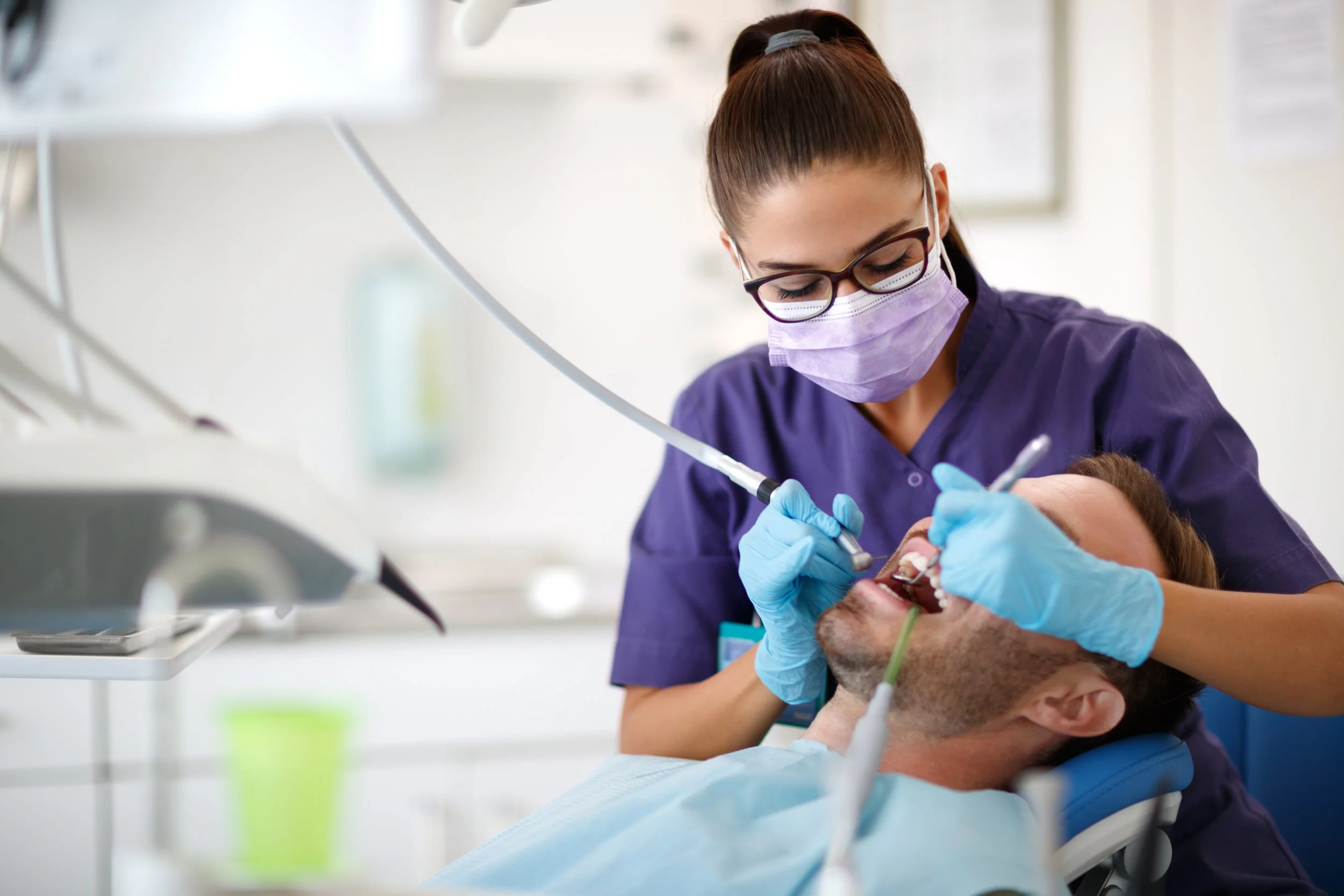 Woman purple scrubs and glasses cleaning the teeth of a patient