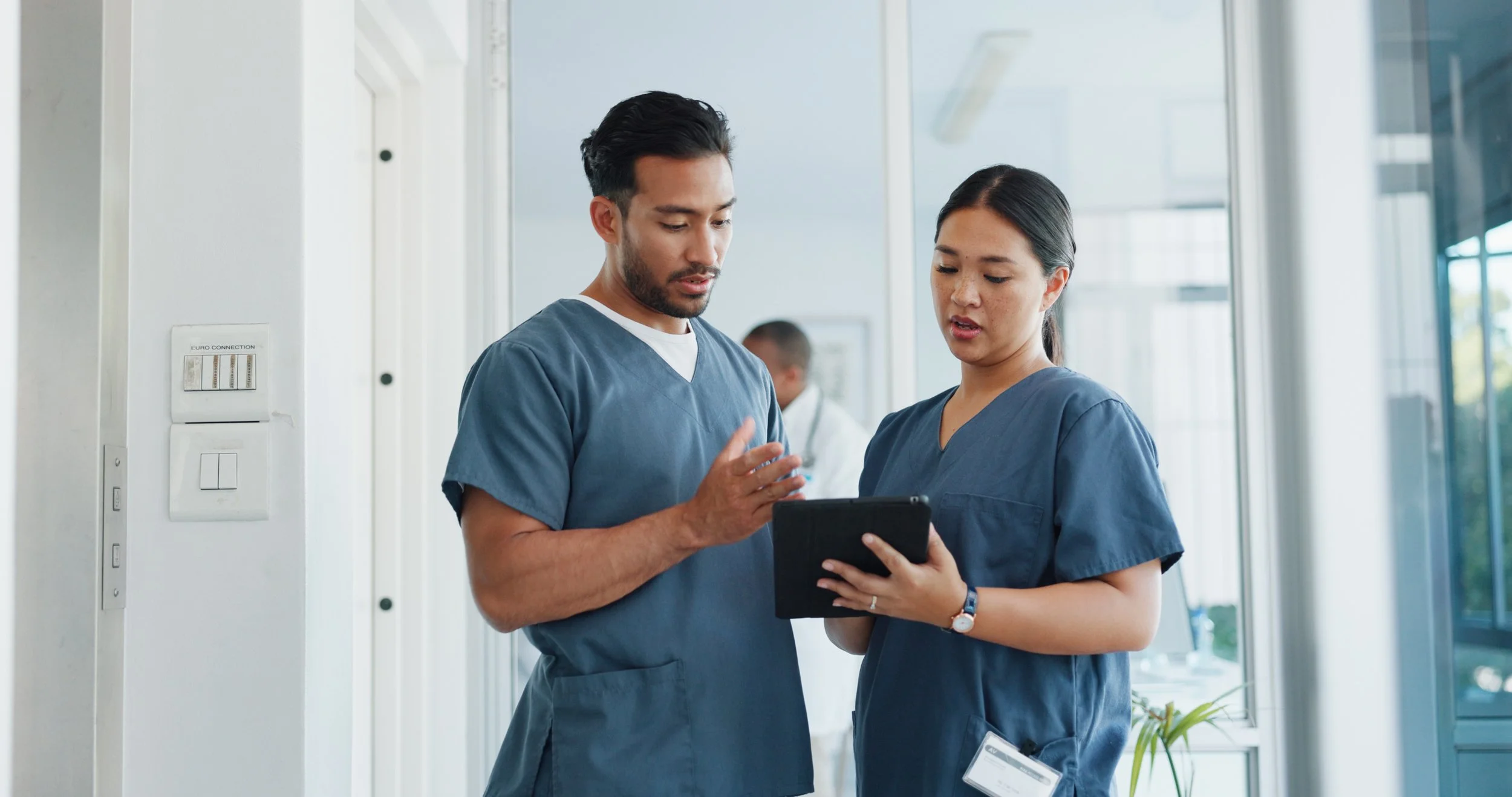 A man and woman in blue scrubs discuss information on a clipboard between them