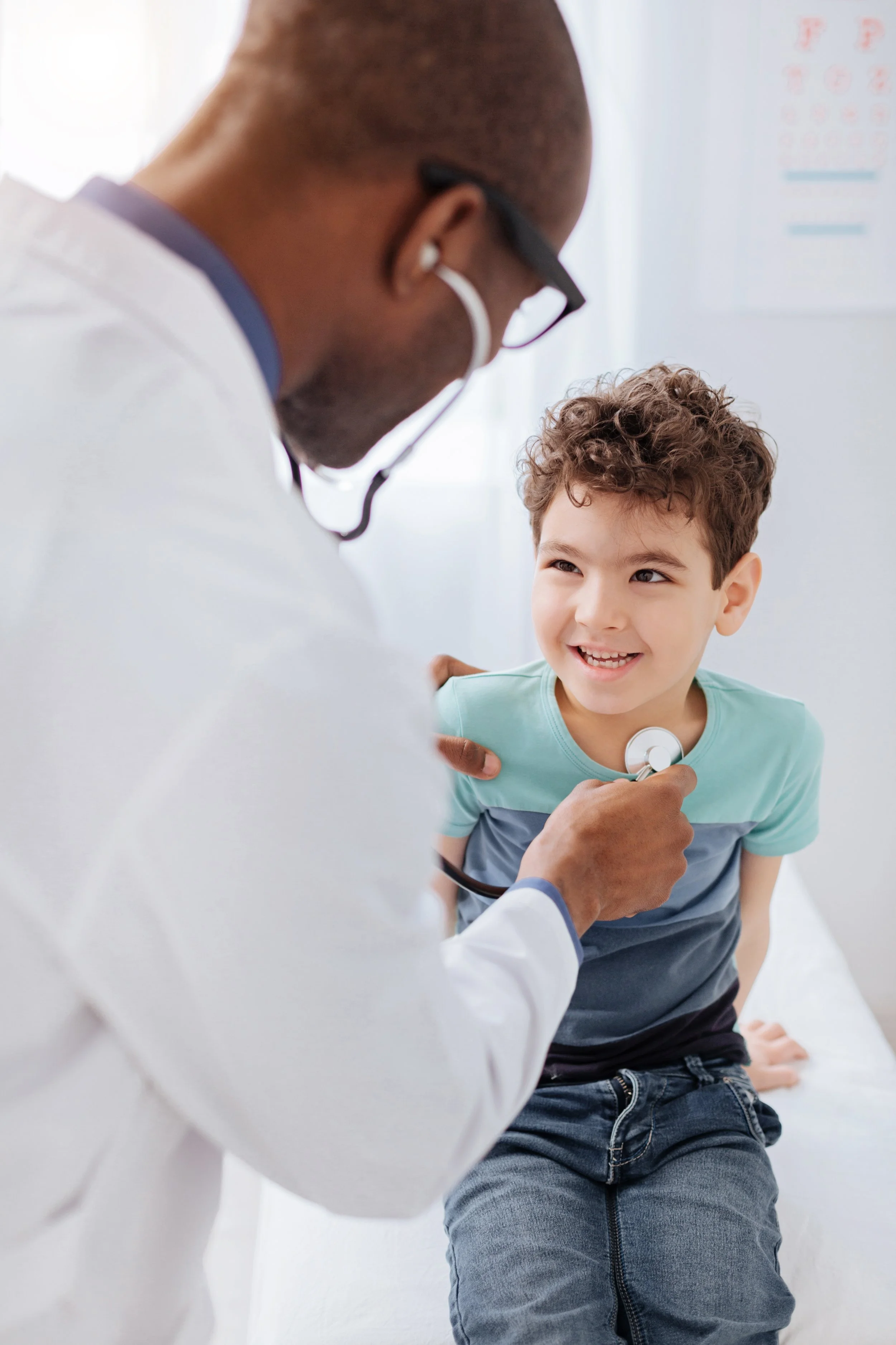Young boy smiles up at the doctor as he checks him with a stethoscope