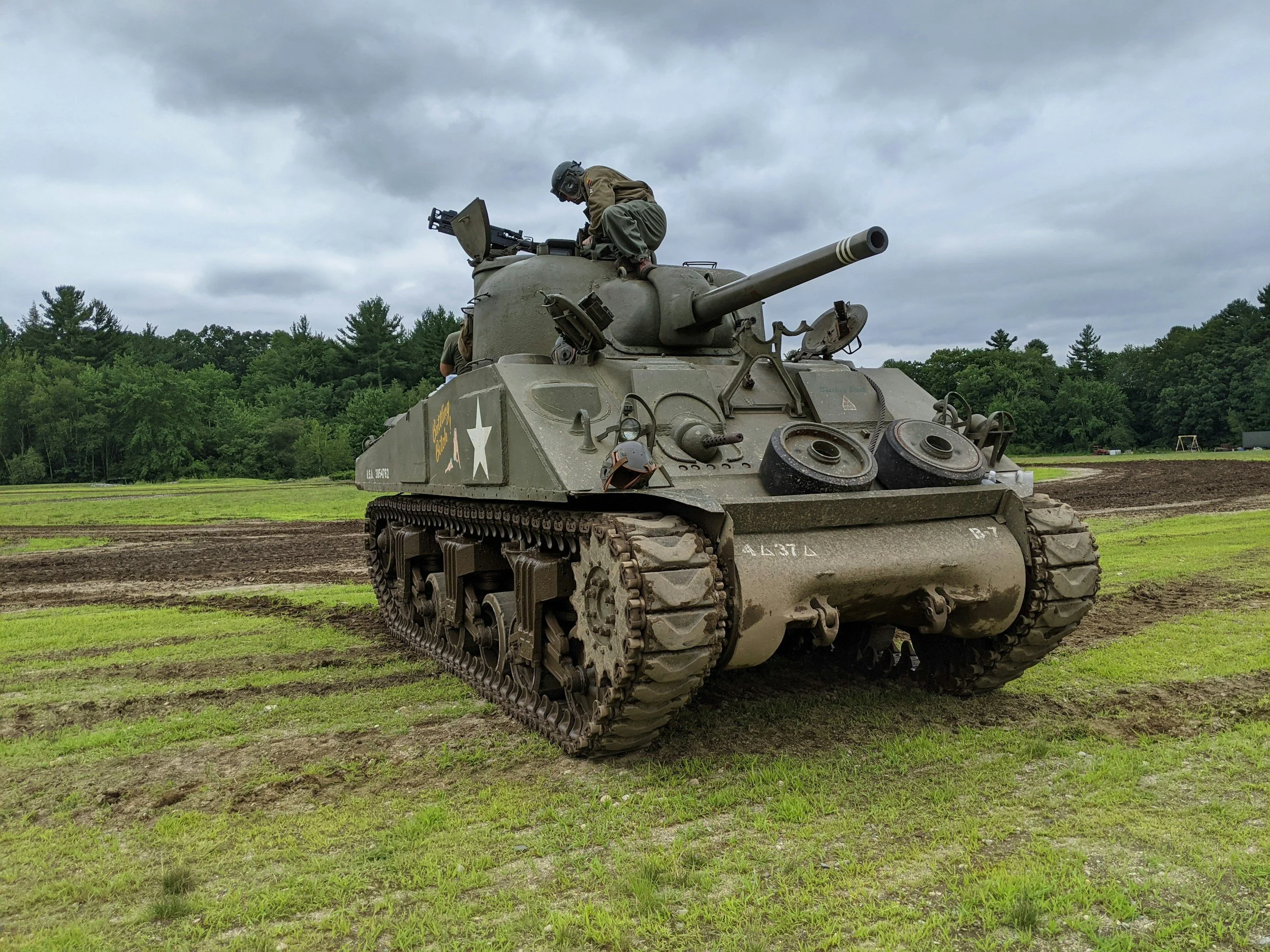 A vintage military tank on grassy field with a soldier