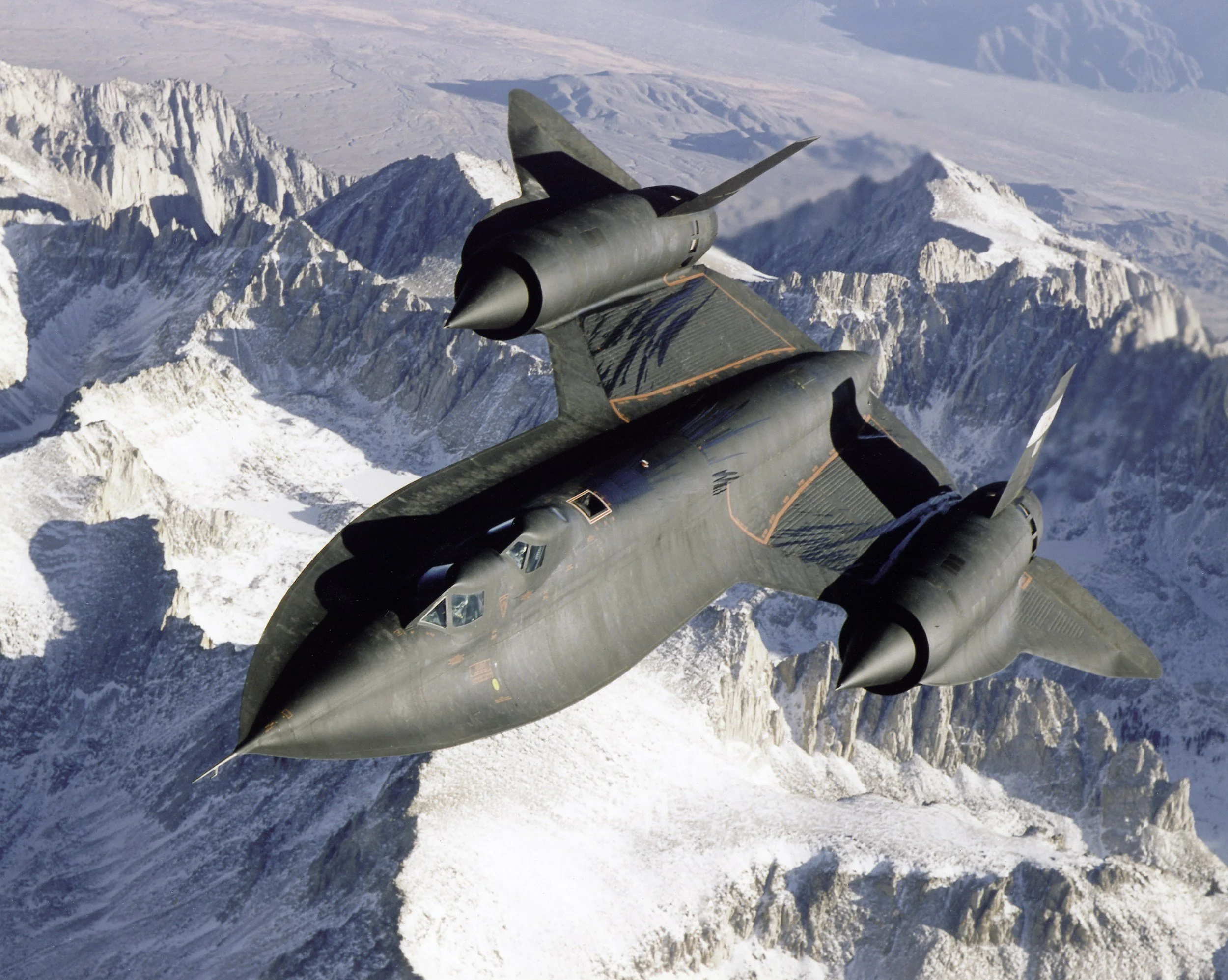 SR-71 Blackbird aircraft flying over snowy mountains.