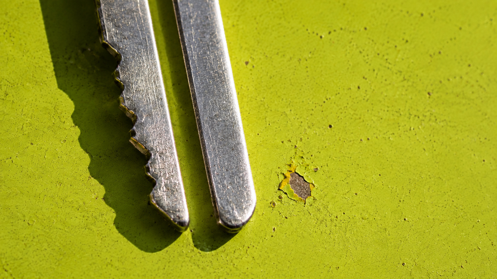 A toothed steel key lies beside a blade filed smooth on chipped acid yellow-green enamel.