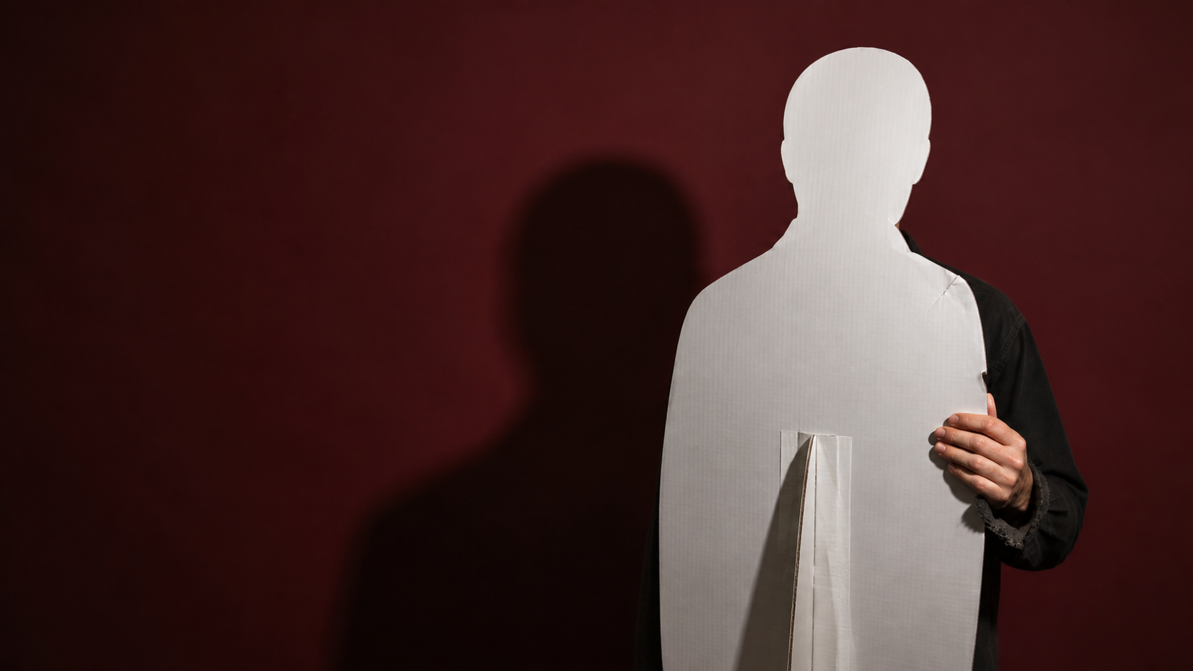 An anonymous adult stands behind a blank human cutout, with a real shoulder and gripping hand visible.