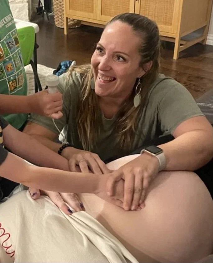 A smiling midwife while she is having the siblings "help" with feeling the baby's position at a prenatal visit.