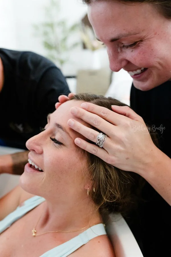 A woman who just had a waterbirth at our midwife-led birth center sits with eyes closed, smiling as her doula gently holds her forehead, both smiling warmly.