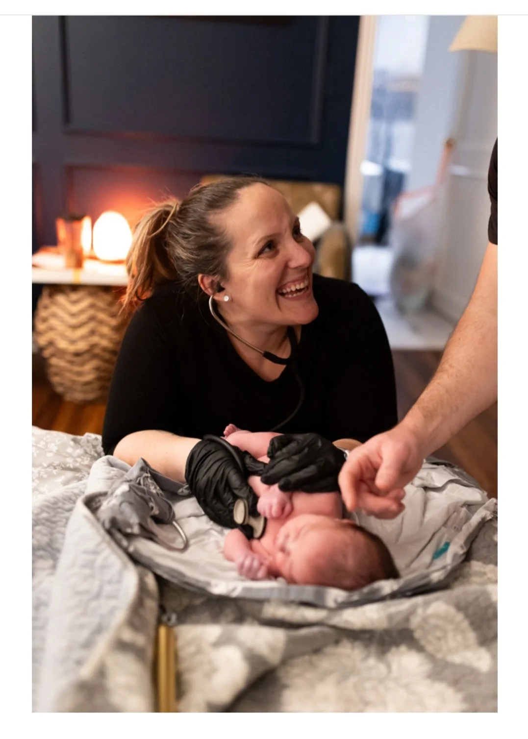 A midwife with a joyful expression, wearing gloves, during the newborn exam a few hours after birth at a home.