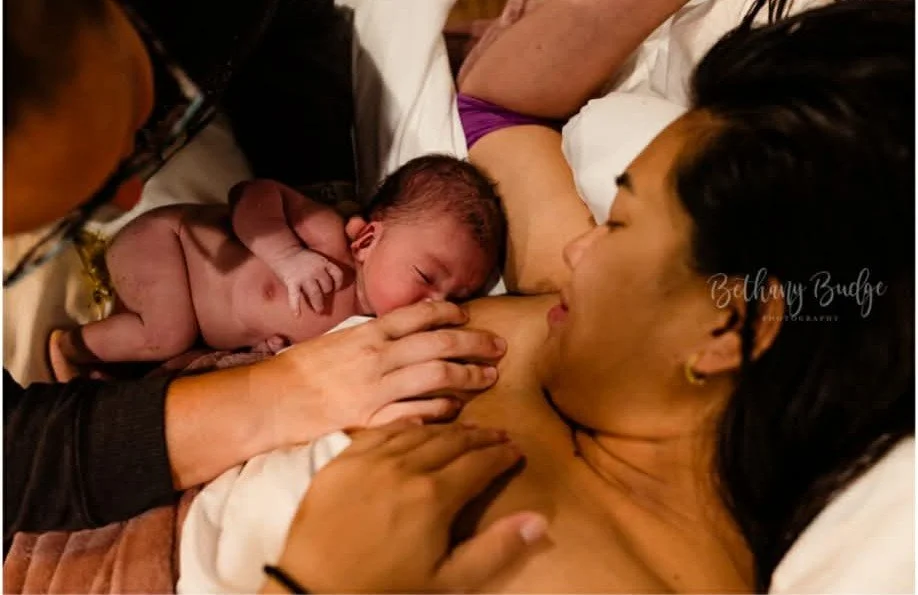 Midwife gently guiding a newborn to breastfeed within the first hour after birth at our Keller, Texas midwife-led birth center, as baby rests skin-to-skin with mother.