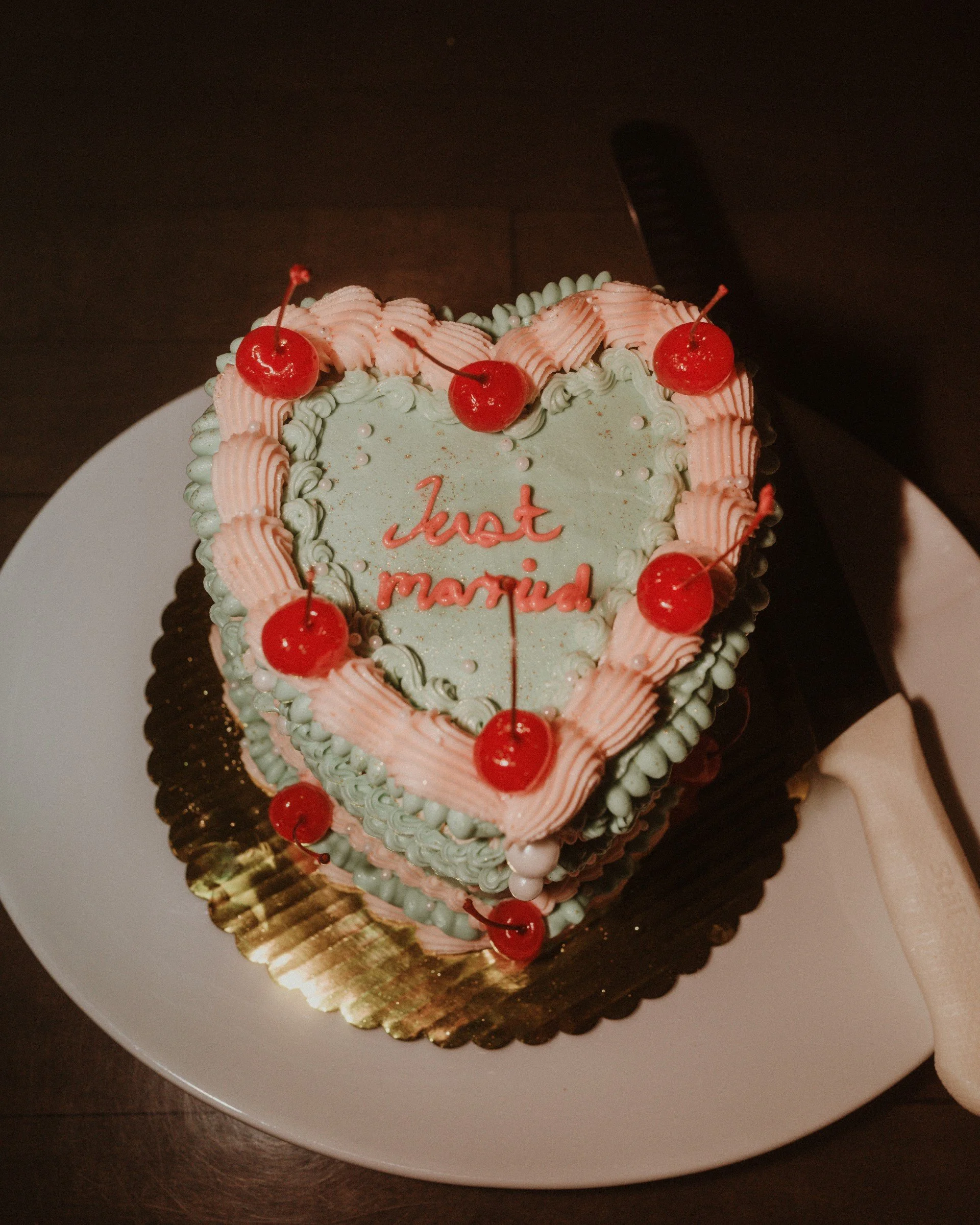 Heart-shaped wedding cake with "Just Married" text, blue frosting, pink icing, and cherries on top.