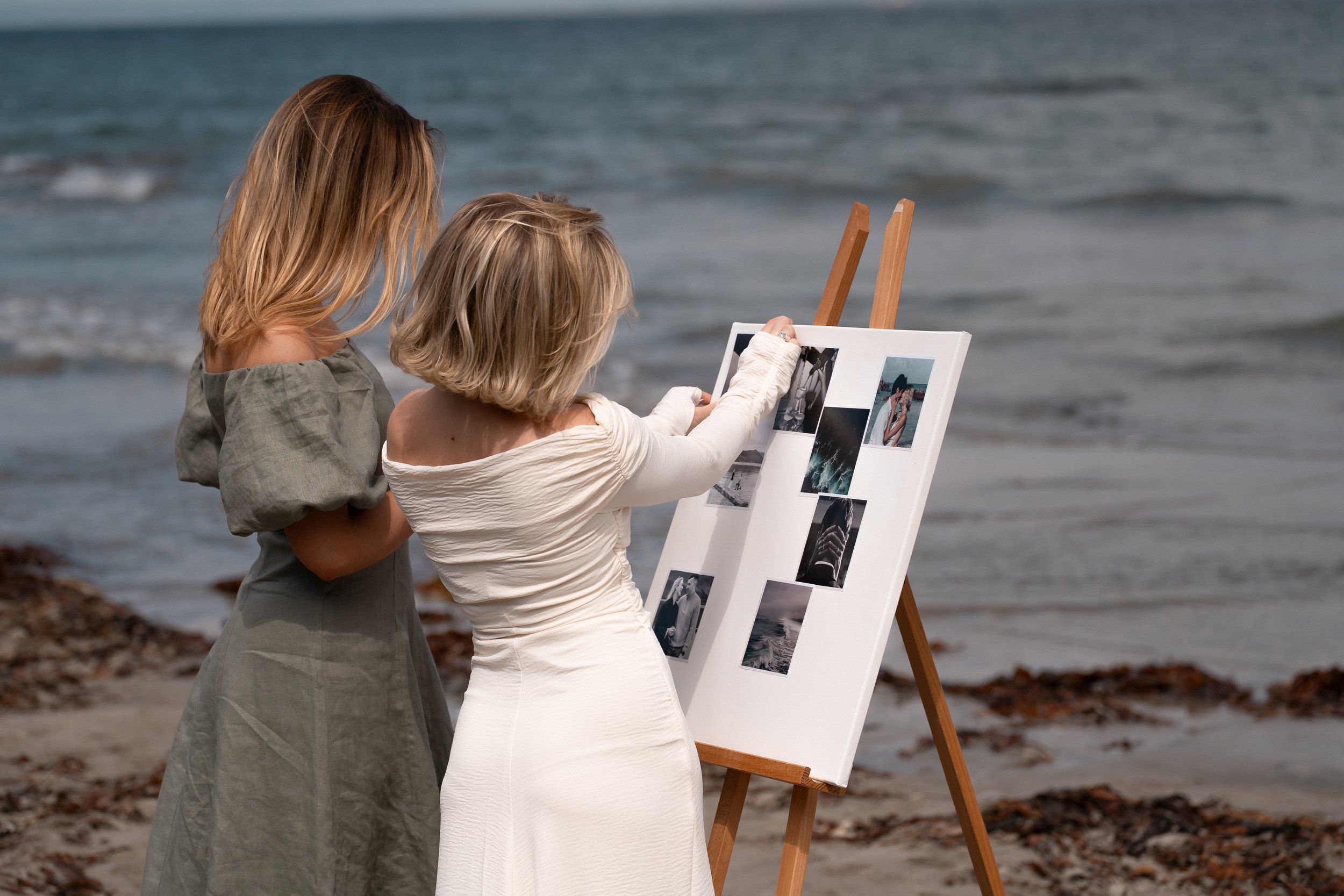 WEDEUX creators standing on a beach looking at photographs on a vision board.