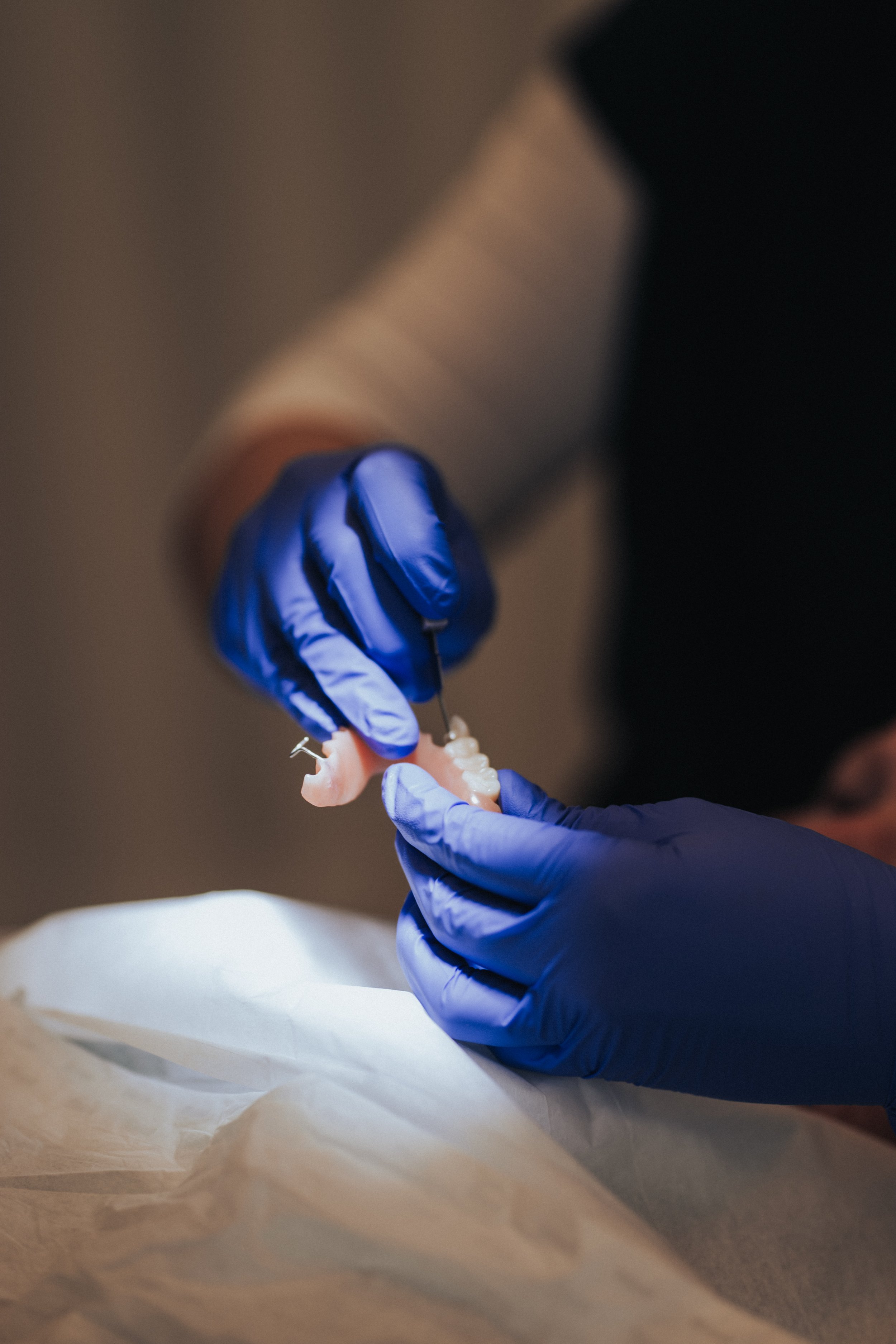 Close-up of a person wearing blue gloves holding a dental prosthetic or mold, preparing for dental work.