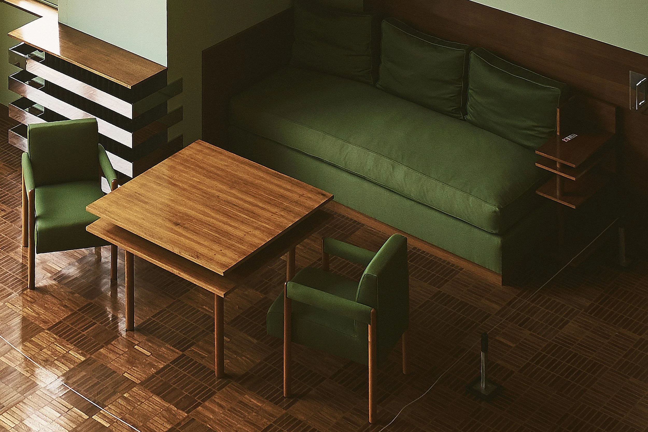 A room with a green sofa, two green chairs, a wooden table, and a wooden side table with shelves, all on a wood parquet floor.