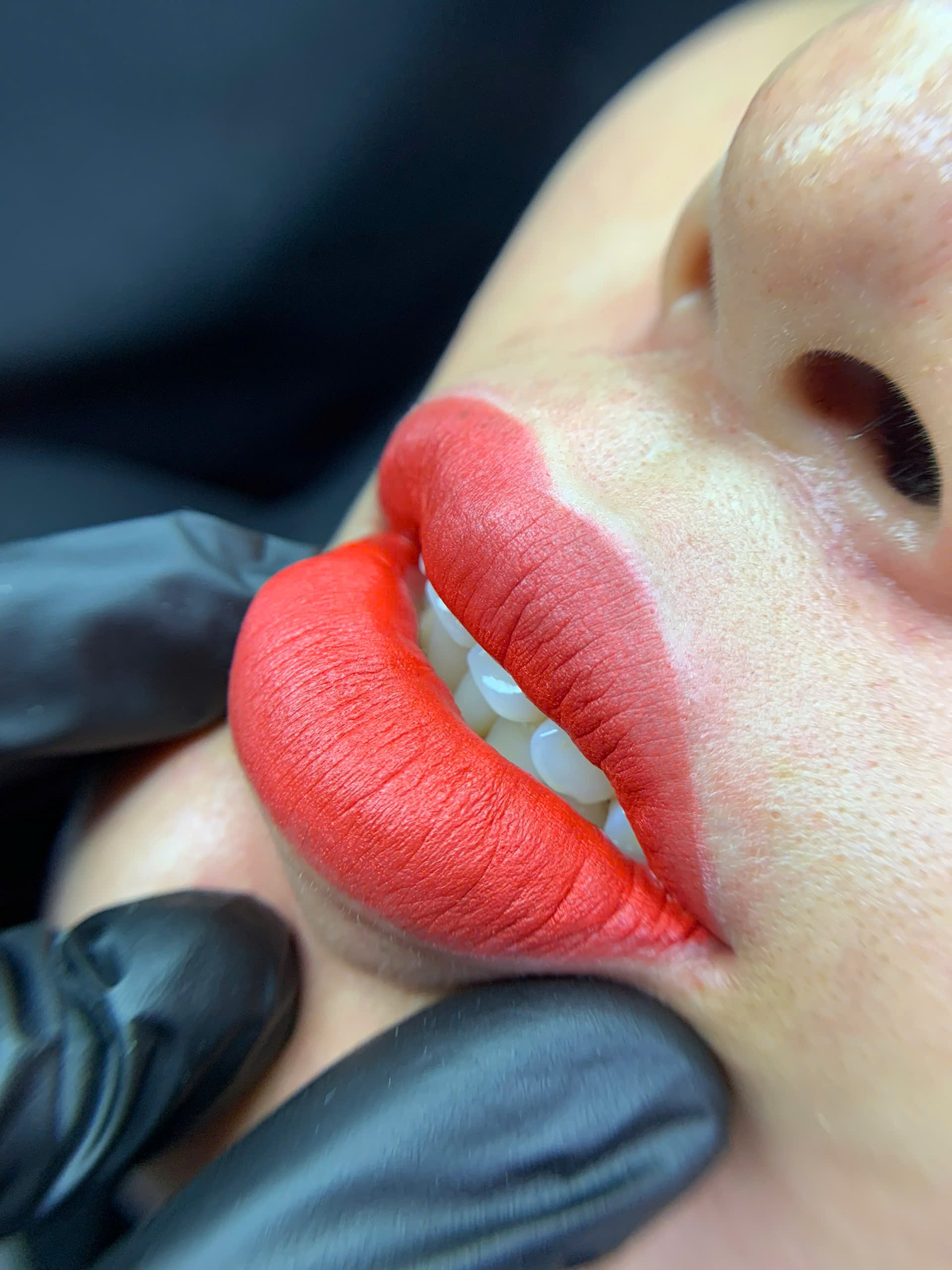 Close-up of lips with bright red lipstick and black gloves touching them
