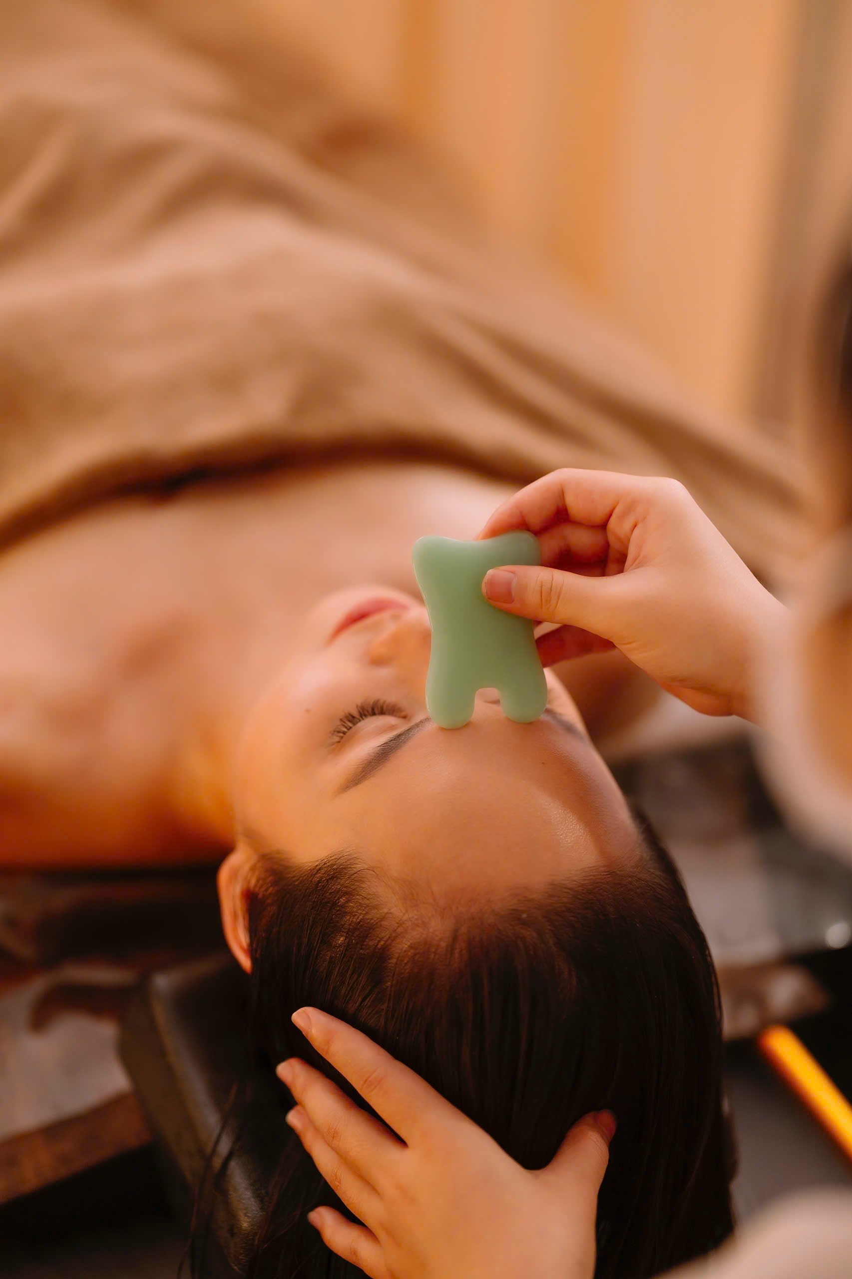 Person receiving a facial massage with a green jade gua sha