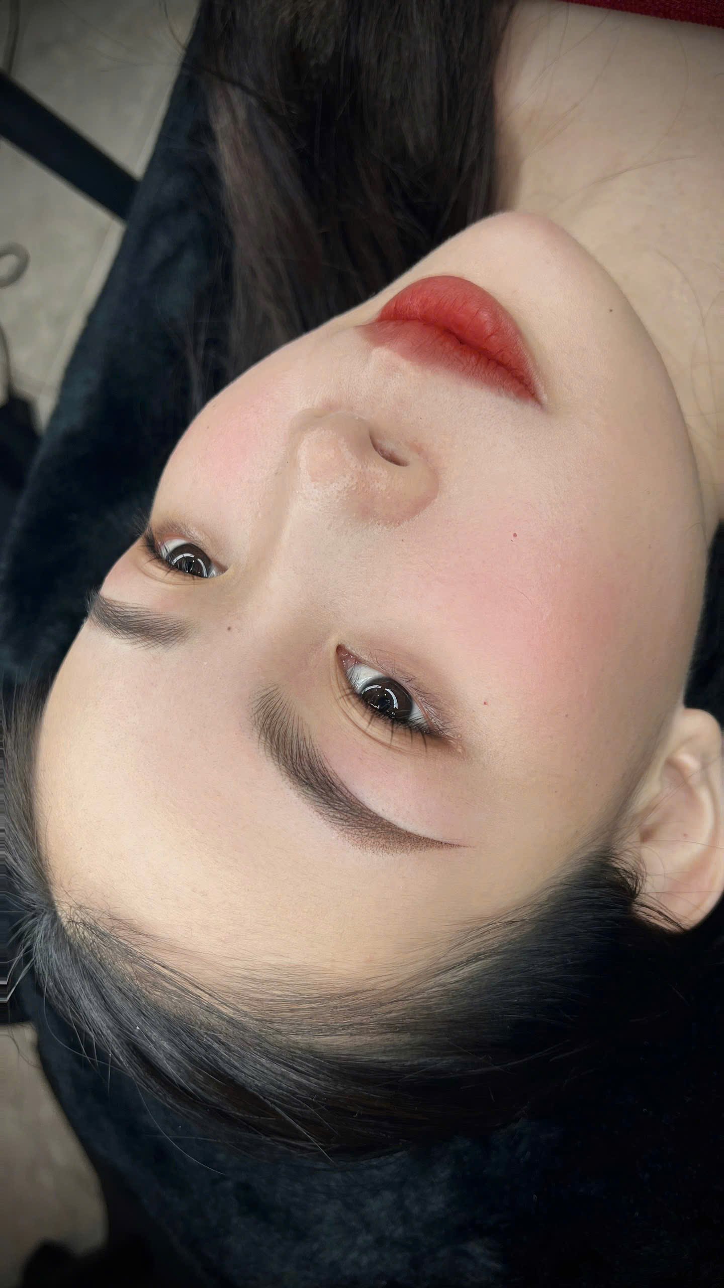 Close-up of a woman lying down with makeup, focusing on eyes and lips.