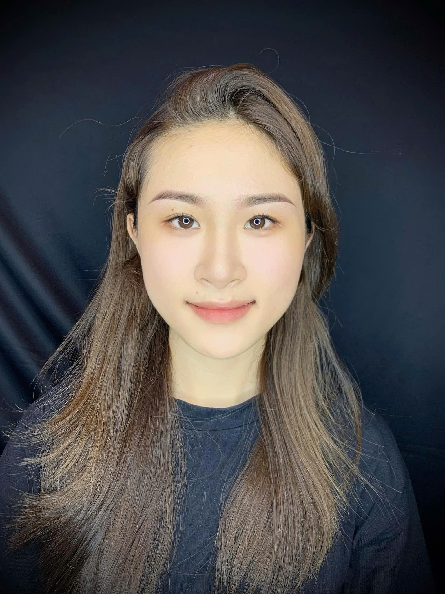 Portrait of a young woman with long, dark brown hair, wearing a black shirt, set against a dark background.