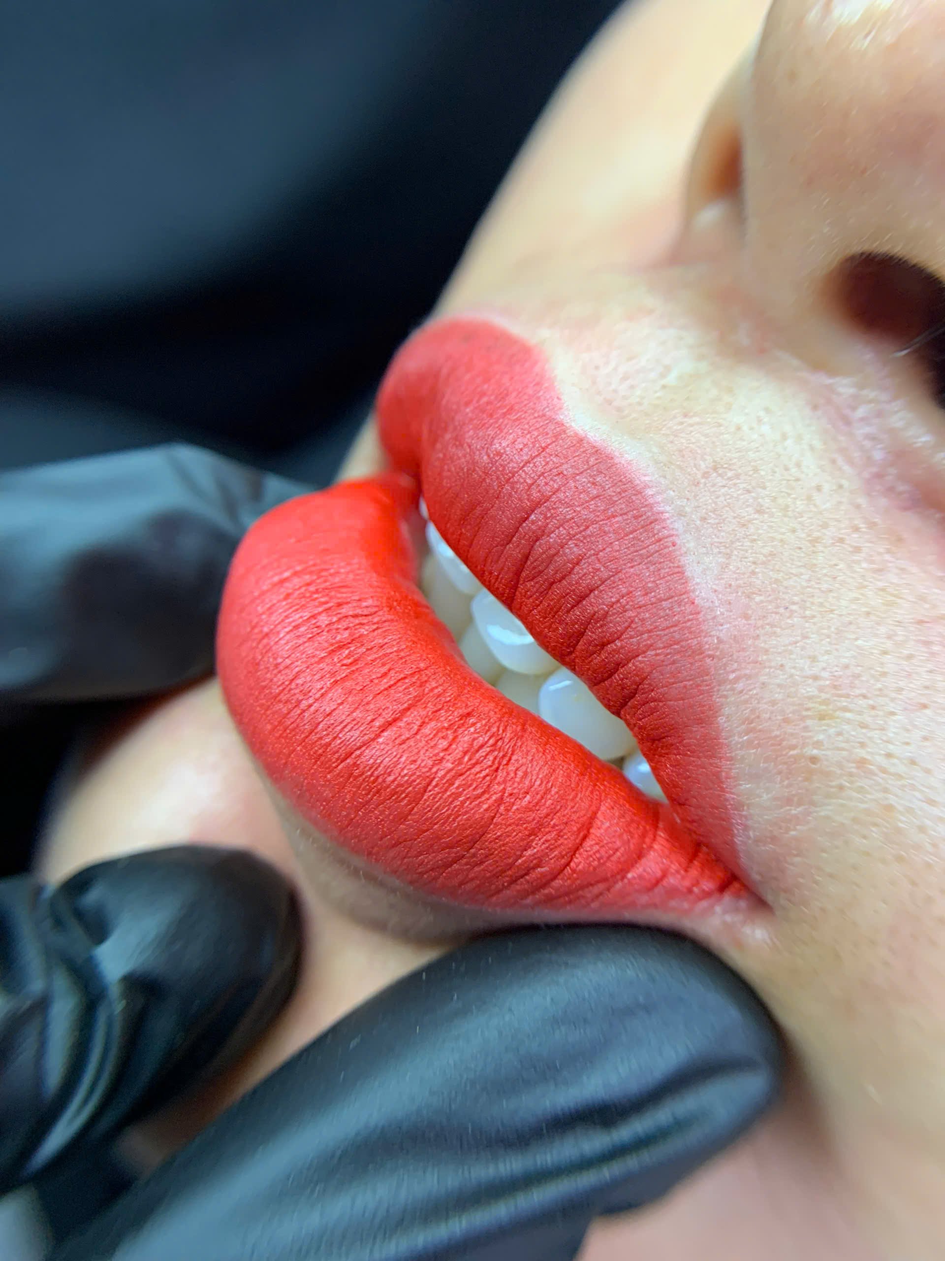Close-up of a person wearing red lipstick, with gloved fingers gently holding their chin, showcasing a lip enhancement or cosmetic procedure.
