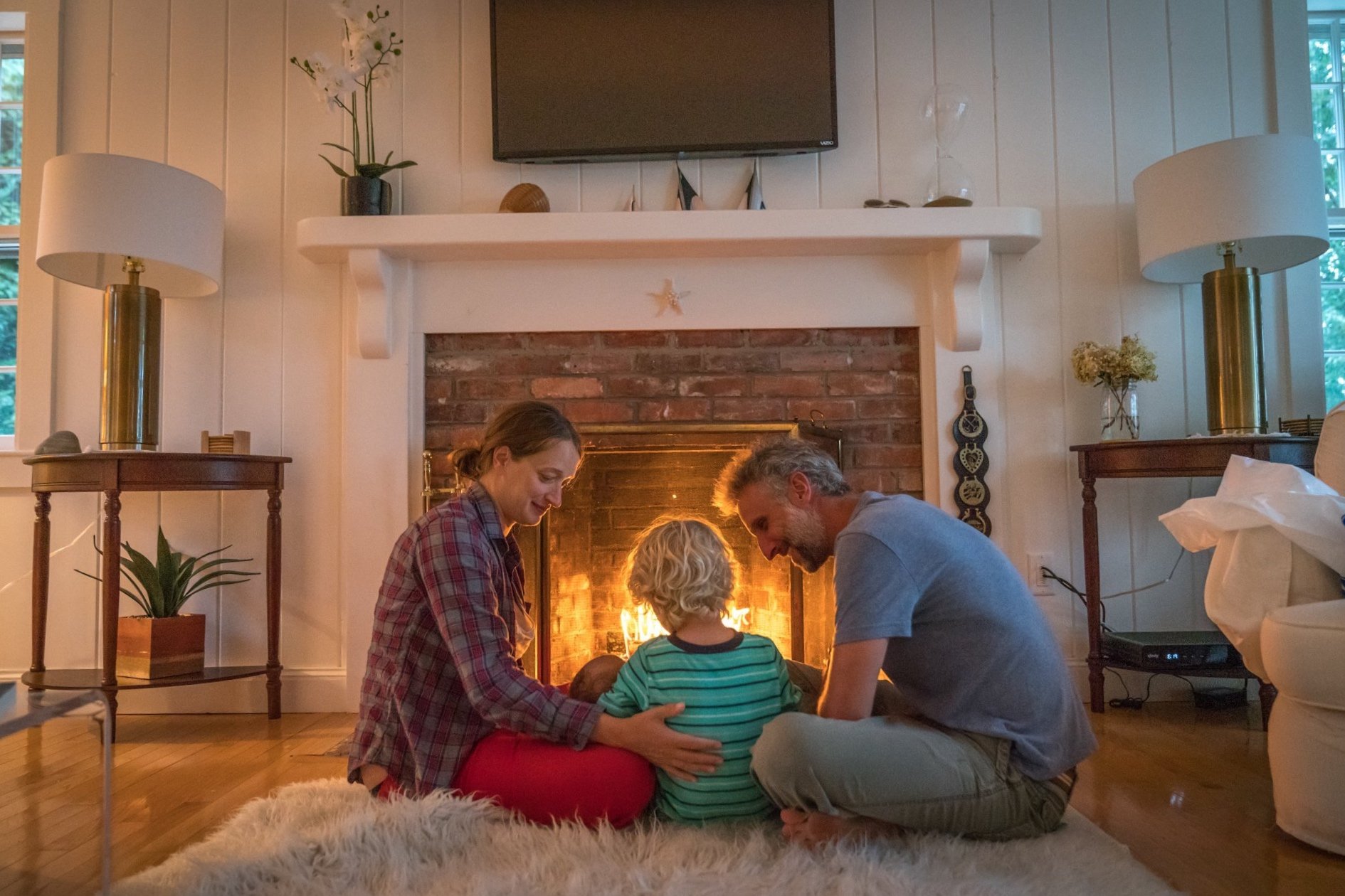 A family sitting together by a fireplace with a fire burning, lovingly embracing and spending time together in a cozy living room.