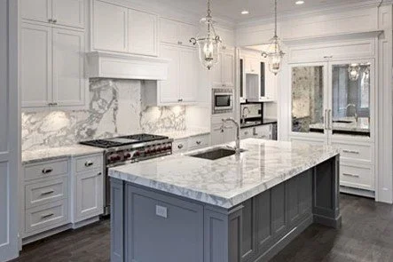 Modern kitchen with white cabinetry, marble countertops, and a large kitchen island with a dark base.