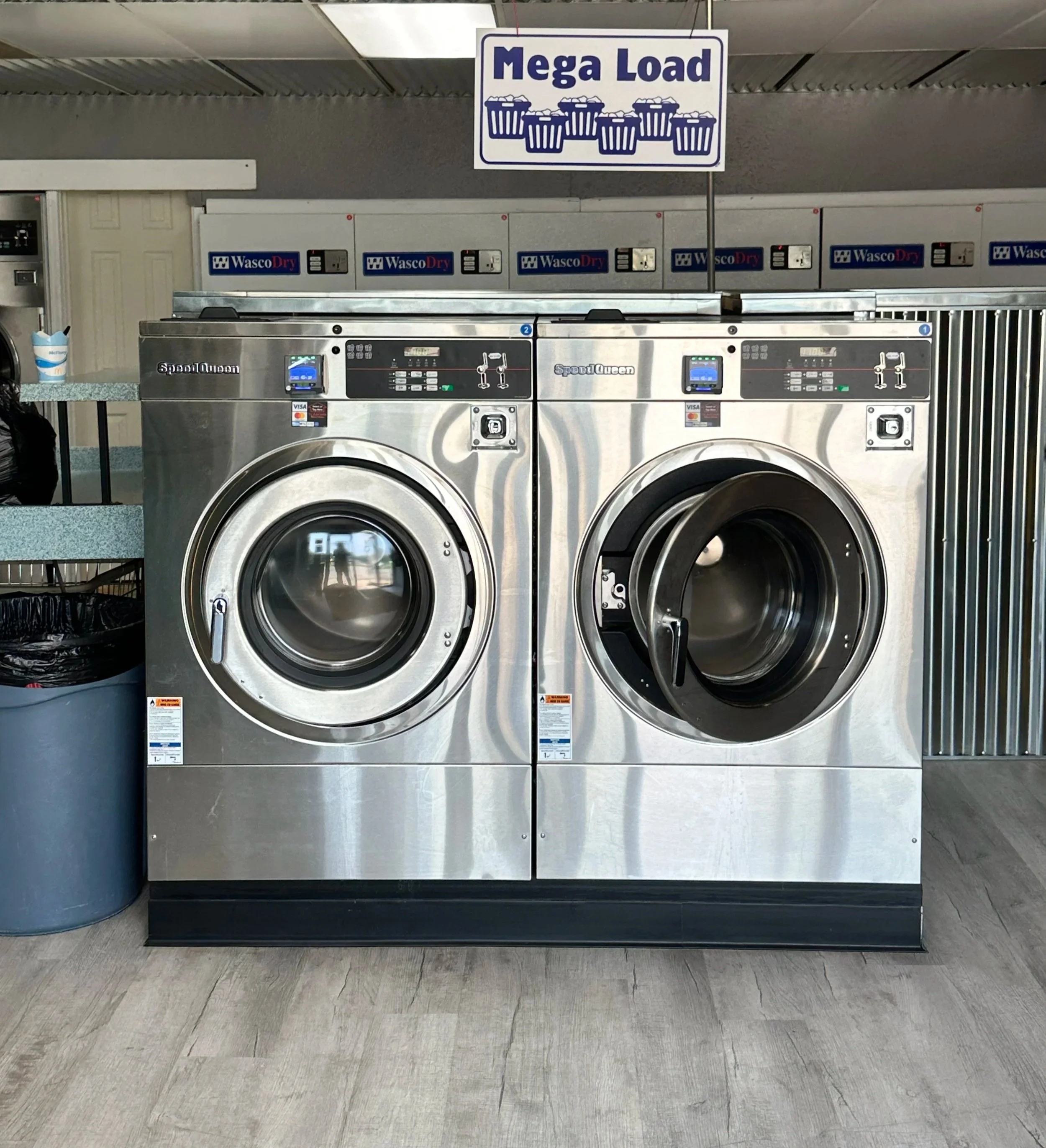 Interior of a laundromat with washing machines, laundry carts, and folding tables.