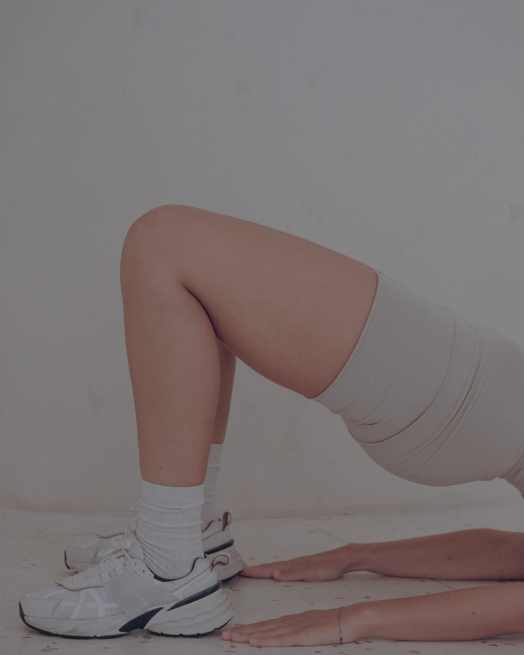 Persona en posición de yoga en interior, apoyada en sus manos y rodillas, usando ropa deportiva blanca, calcetas y zapatillas