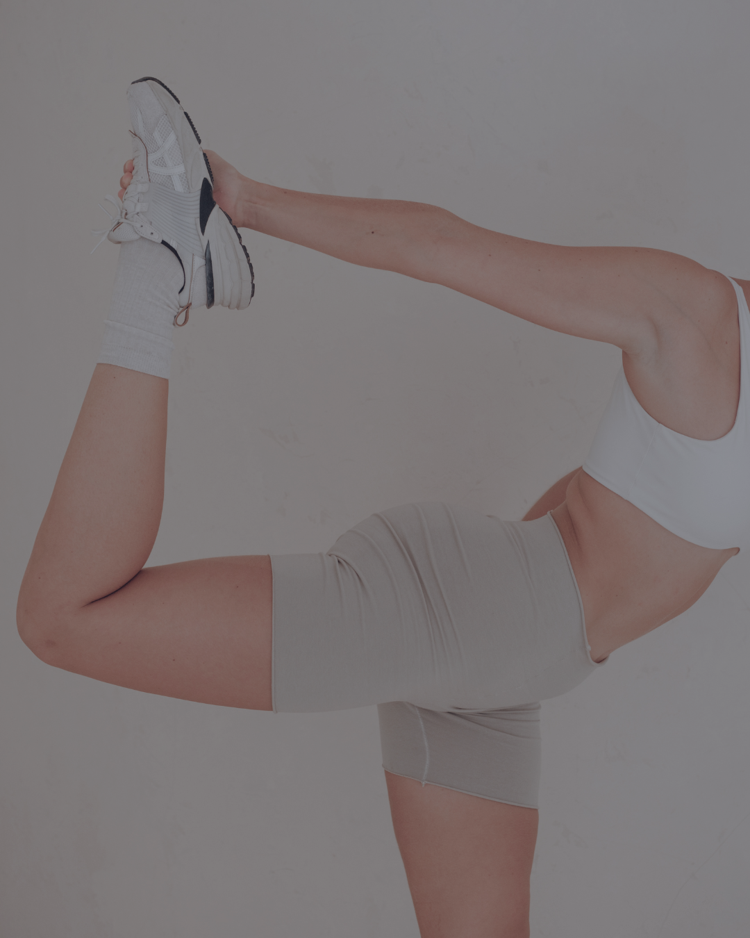 Persona en postura de yoga realizando una postura de equilibrio con una pierna levantada y el brazo extendido, usando ropa deportiva y zapatillas.