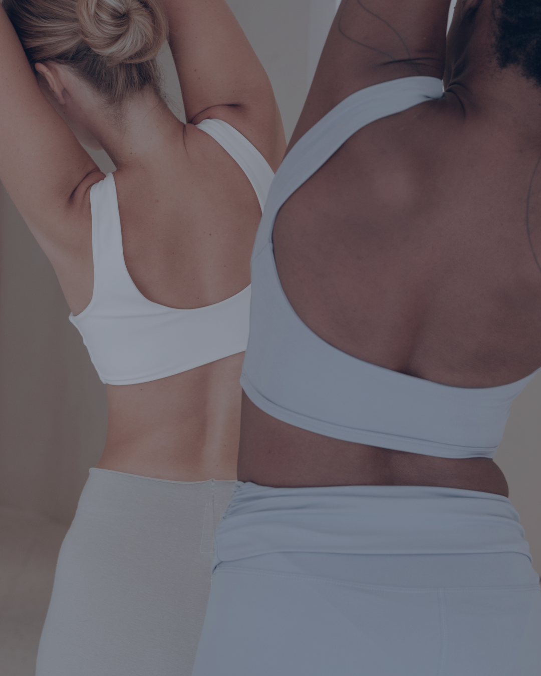 Dos mujeres en ropa deportiva haciendo estiramientos o ejercicio en un gimnasio.