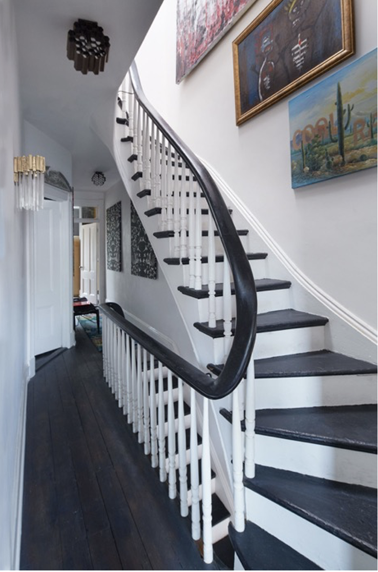 Curved staircase with black steps and white railings, artwork on walls, and dark wood flooring in hallway. Residential Design, Renovation, Restoration, Interior Design and Decor, Art Curation Hope Misterek