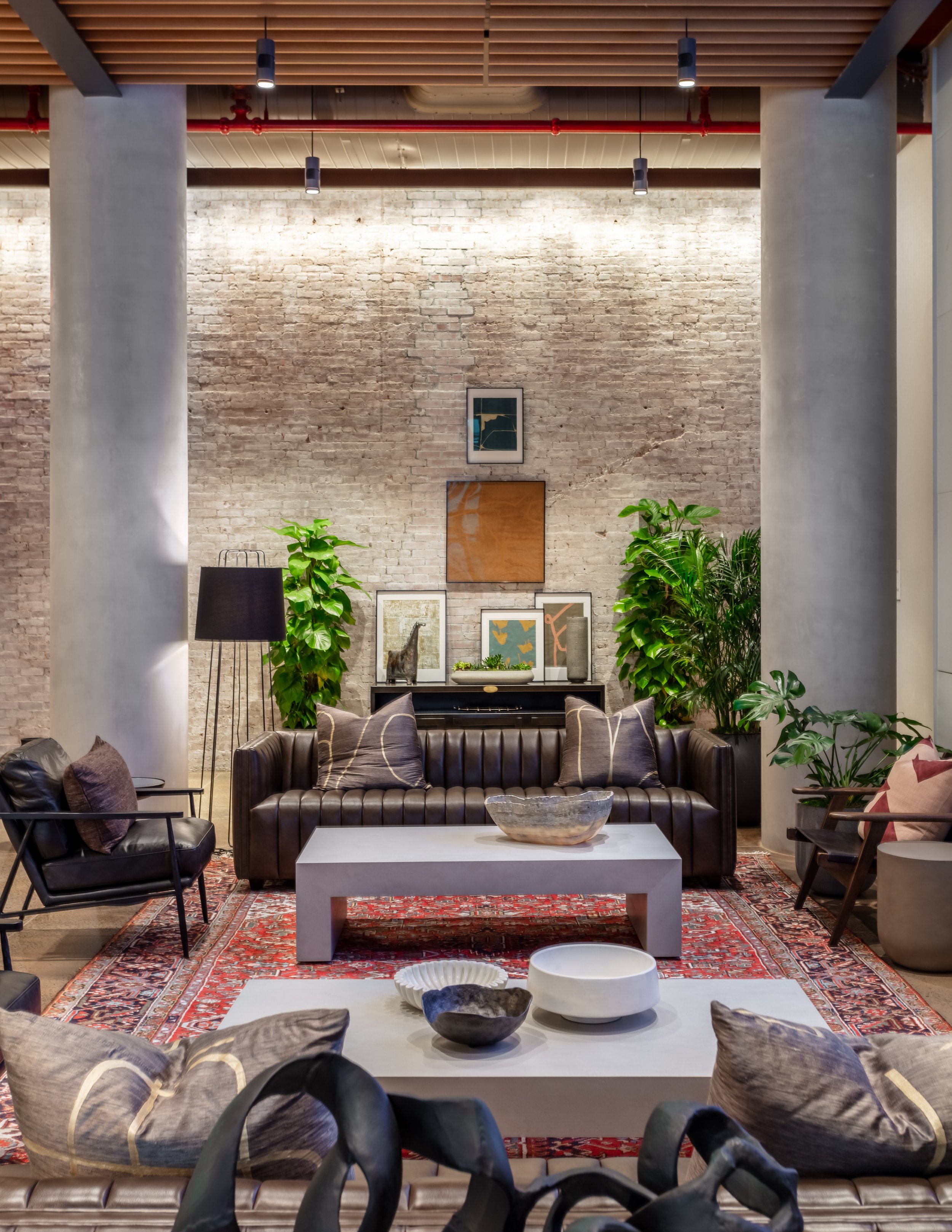 Modern living room with brick walls, leather sofa, rug, coffee tables, indoor plants, and framed art. Interior Furnishings, Decor, Accessories and Art, Design, Procurement, Hope Misterek Art Curation
