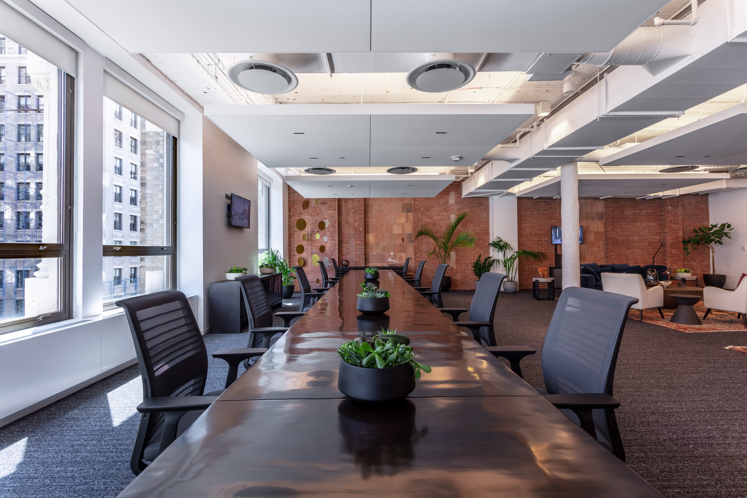 Modern office interior with long conference table, ergonomic chairs, potted plants, large windows, and exposed brick walls. Interior Furnishings, Decor, Accessories and Art, Design, Procurement, Hope Misterek