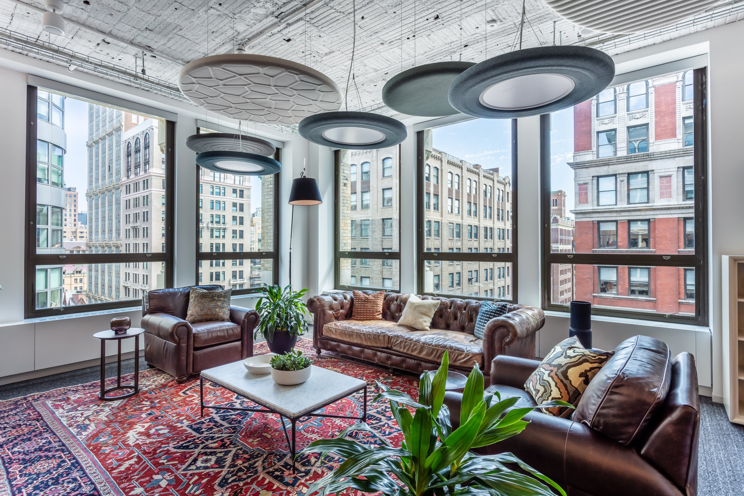 Modern office lounge with large windows, leather sofas, armchairs, coffee table, plants, and acoustic ceiling panels. Interior Furnishings, Decor, Accessories and Art, Design, Procurement, Hope Misterek