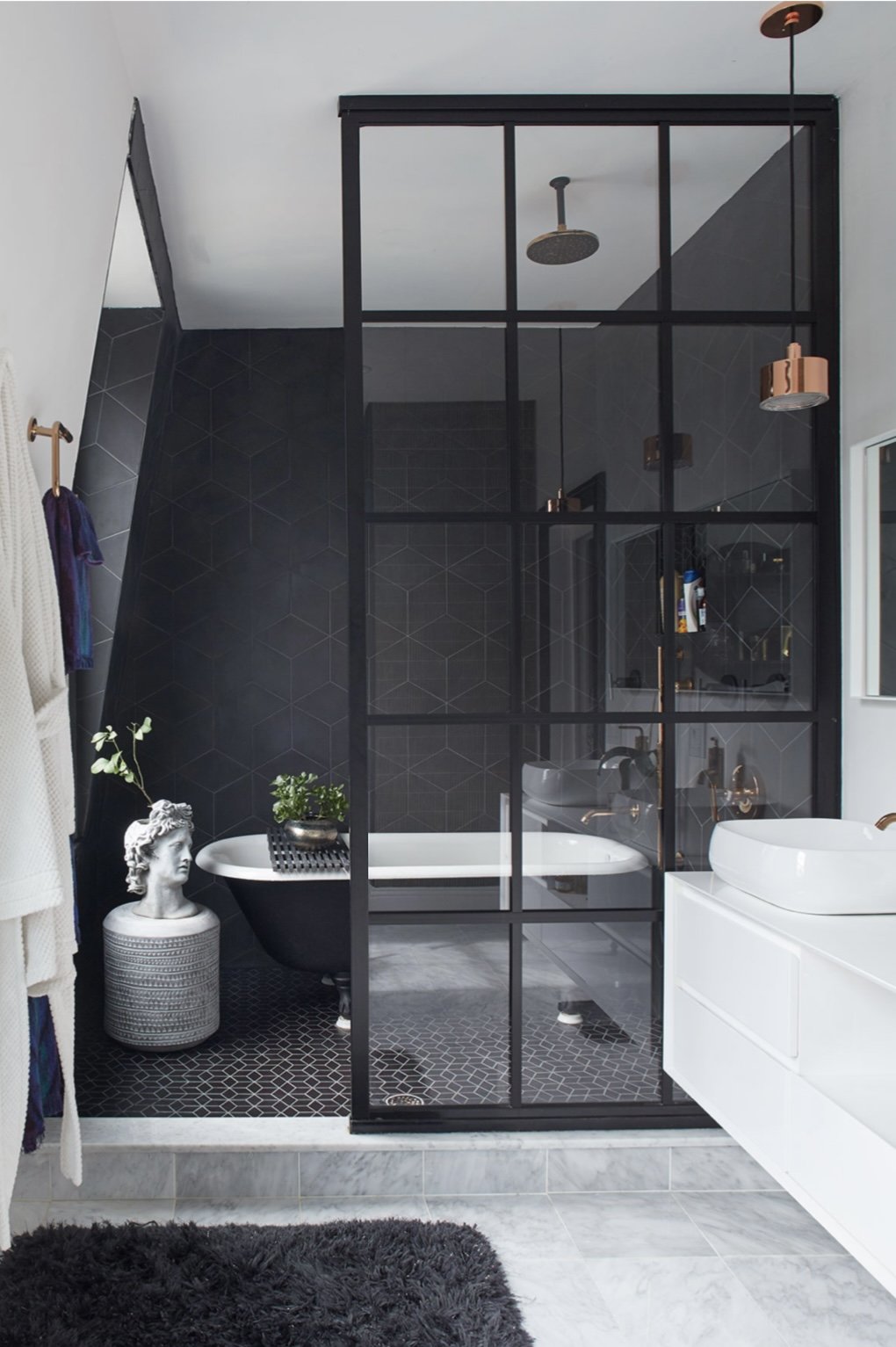Modern bathroom with glass partition, freestanding bathtub, decorative bust, plants, hexagonal tiles, and black accents. Residential Design, Renovation, Restoration, Interior Design and Decor, Art Curation Hope Misterek