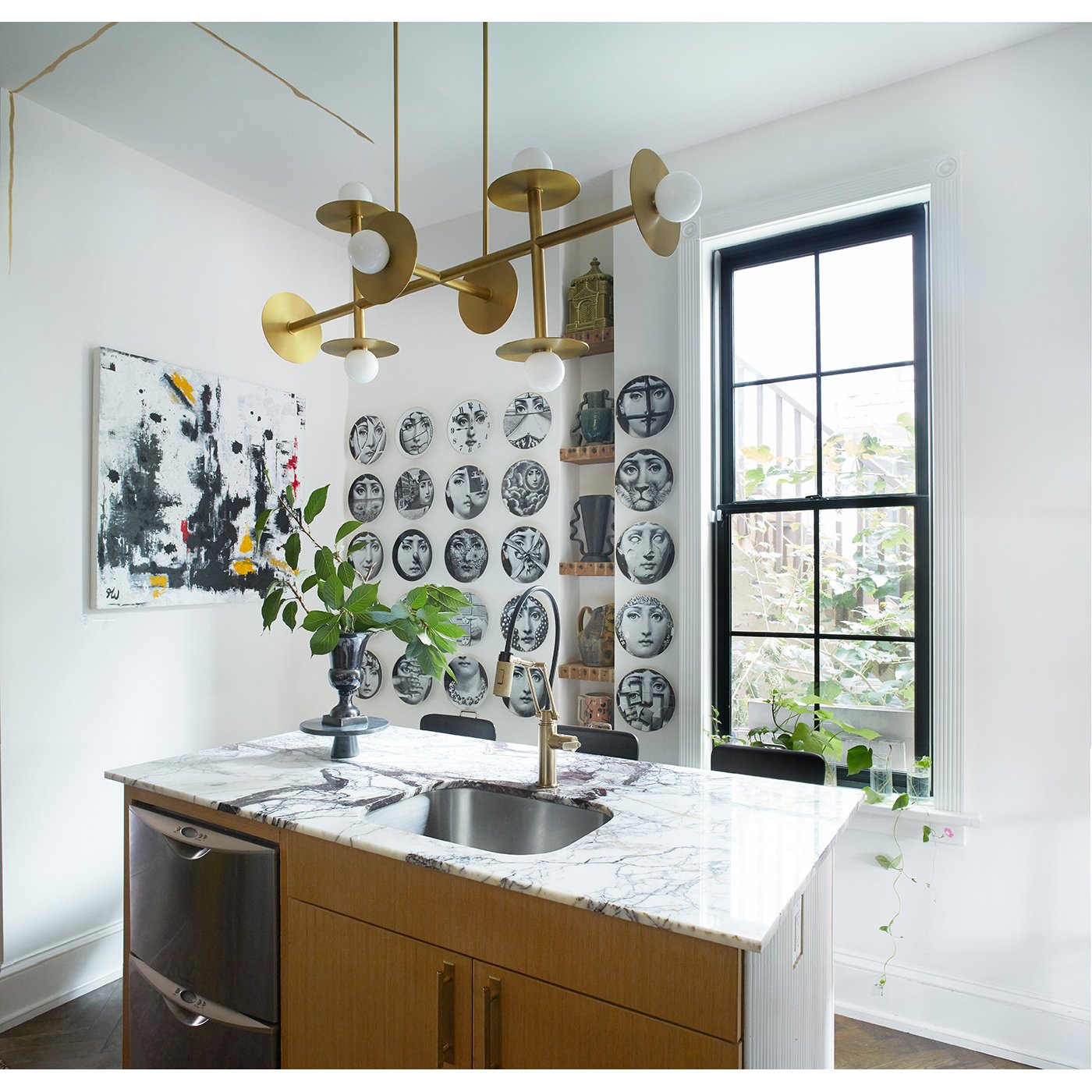 Modern kitchen interior with marble island countertop, gold lighting fixture, and wall art including abstract paintings and decorative plates. Large window with plants adds natural light. Residential Design, Renovation, Restoration, Interior Design a