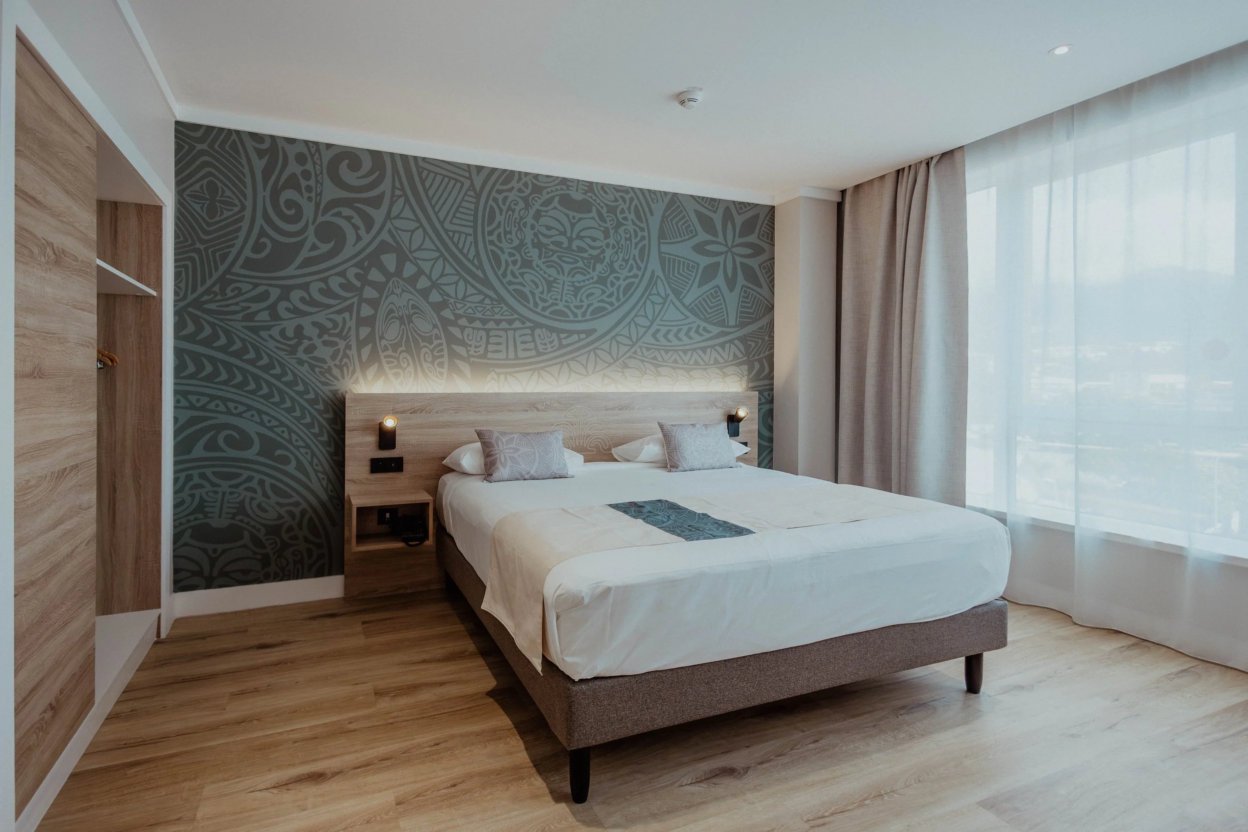 Lits faits avec des oreillers à motifs dans une chambre avec tête de lit en bois et décoration murale.