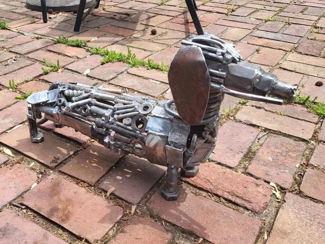 Statue of a dog made from metal parts on a brick patio.